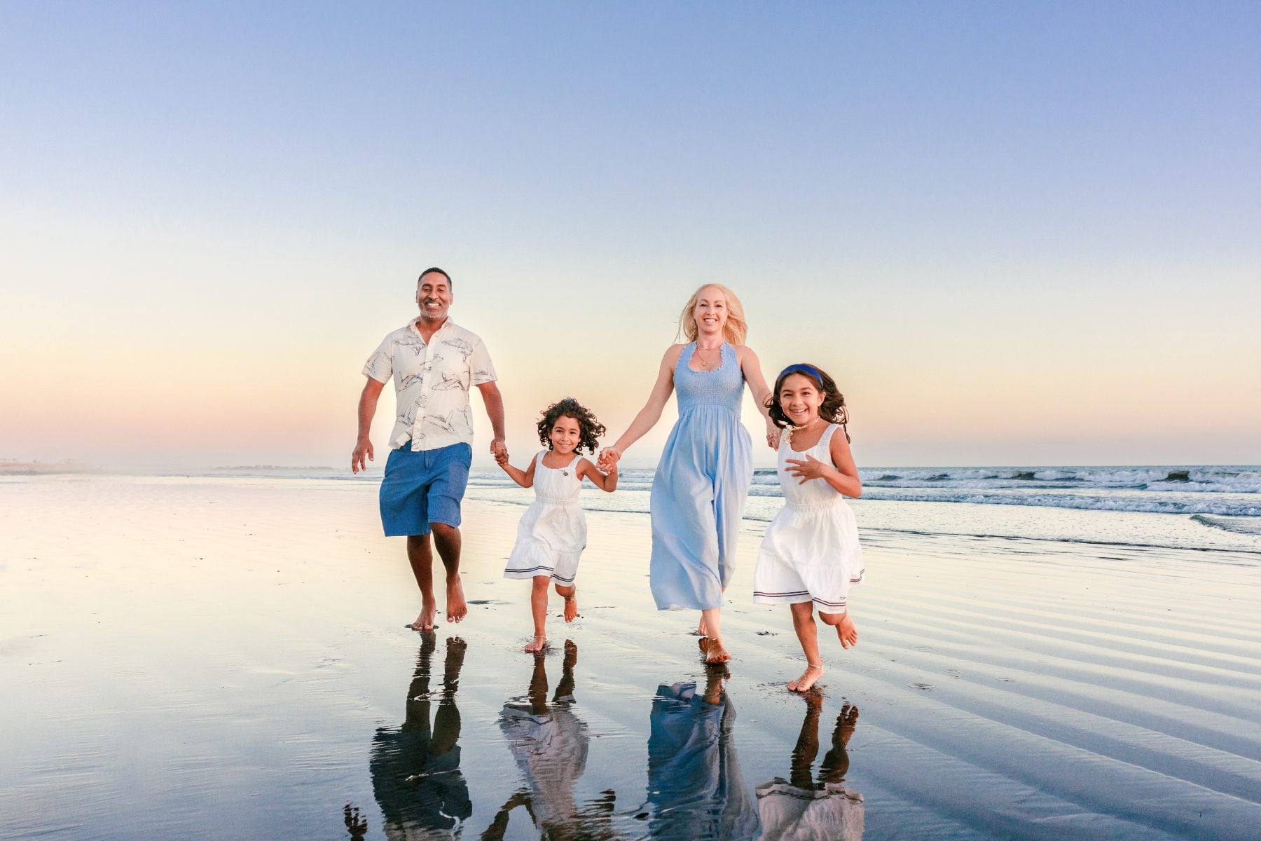 Family of four walking hand in hand along the shoreline, beach family photos San Diego