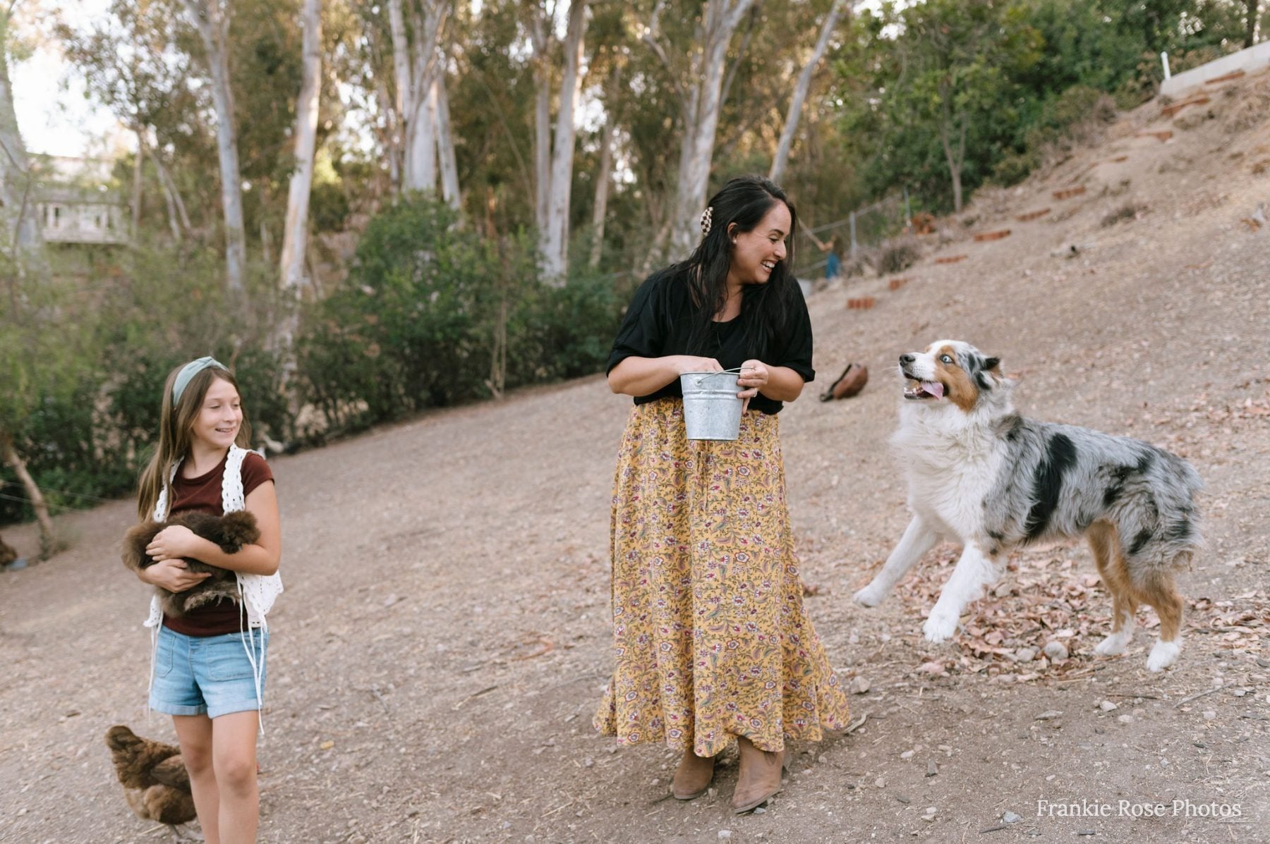 Two women and a girl walk an Australian shepherd on a wooded Lakeside trail
