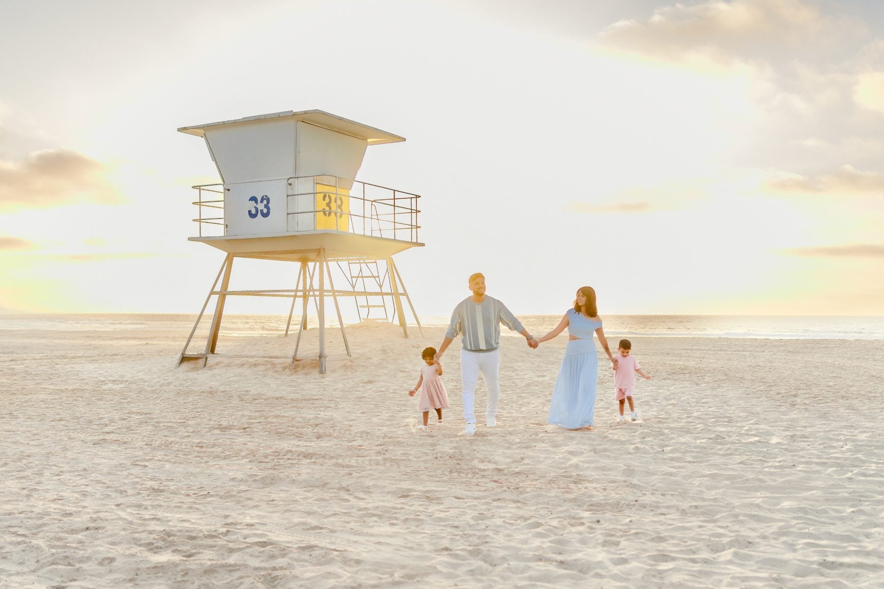 Family of four walks hand-in-hand toward lifeguard tower on La Jolla beach