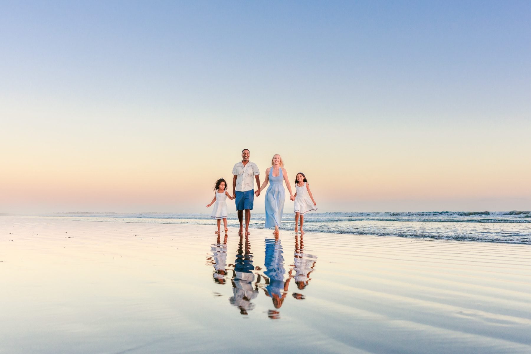 Family of four walks along Coronado Beach at sunset with mirror reflections
