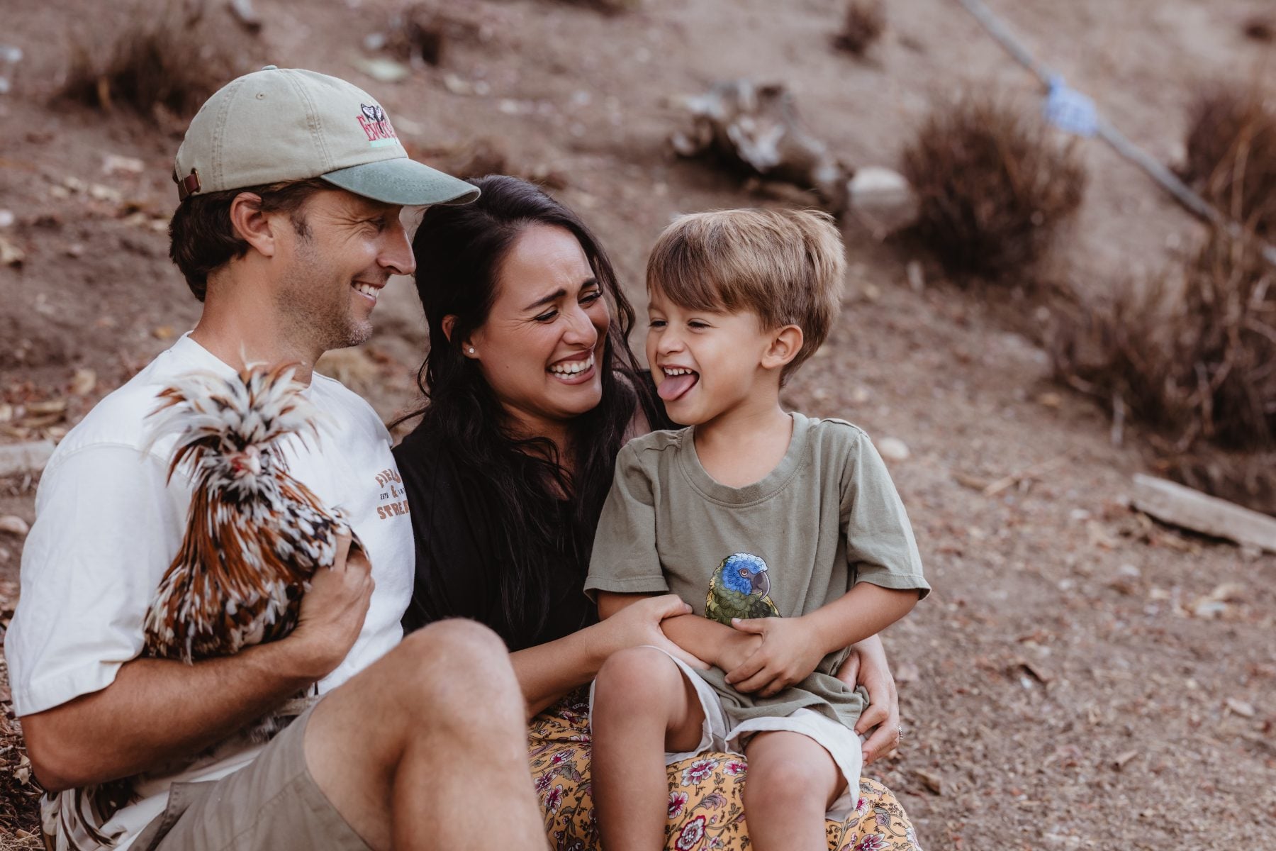 Dad holding a rooster laughs with mom and son outdoors in Lakeside