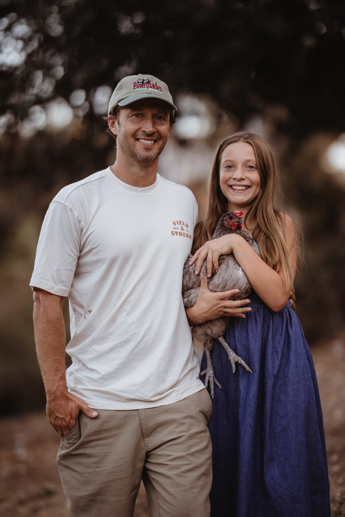 Father and daughter smile while holding a chicken together