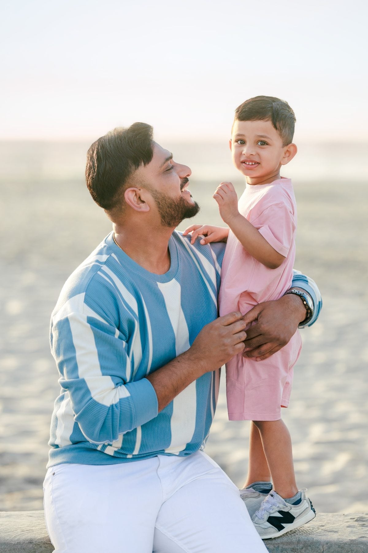 Dad holds young son close, both laughing on the beach