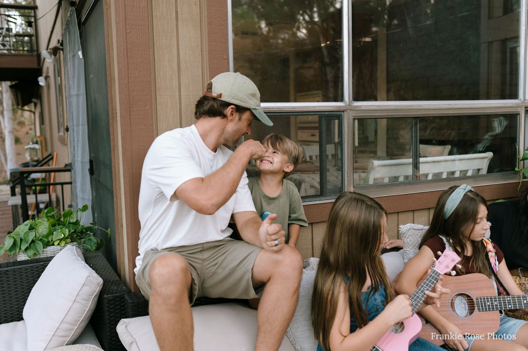 Dad tickling laughing son while two daughters play ukulele nearby
