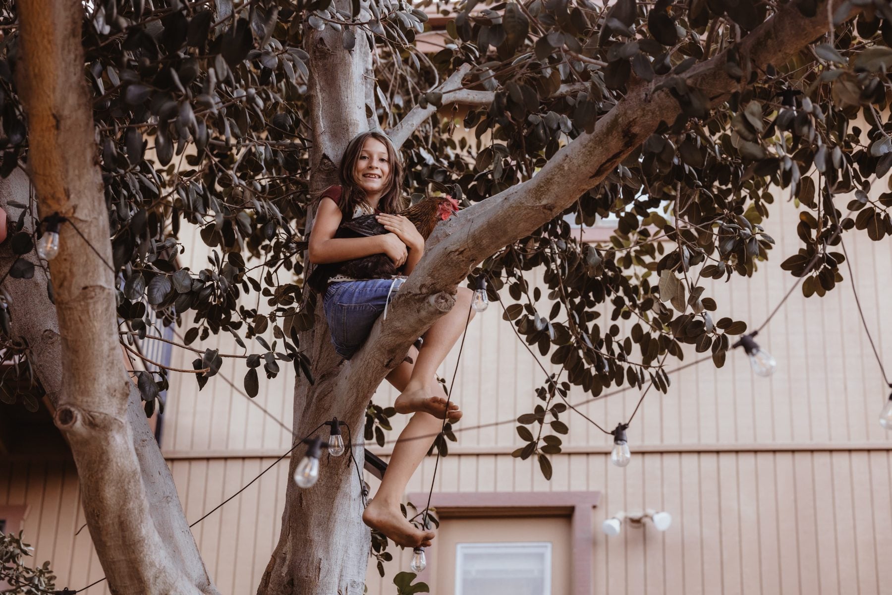 Girl smiles perched high in tree branches strung with lights