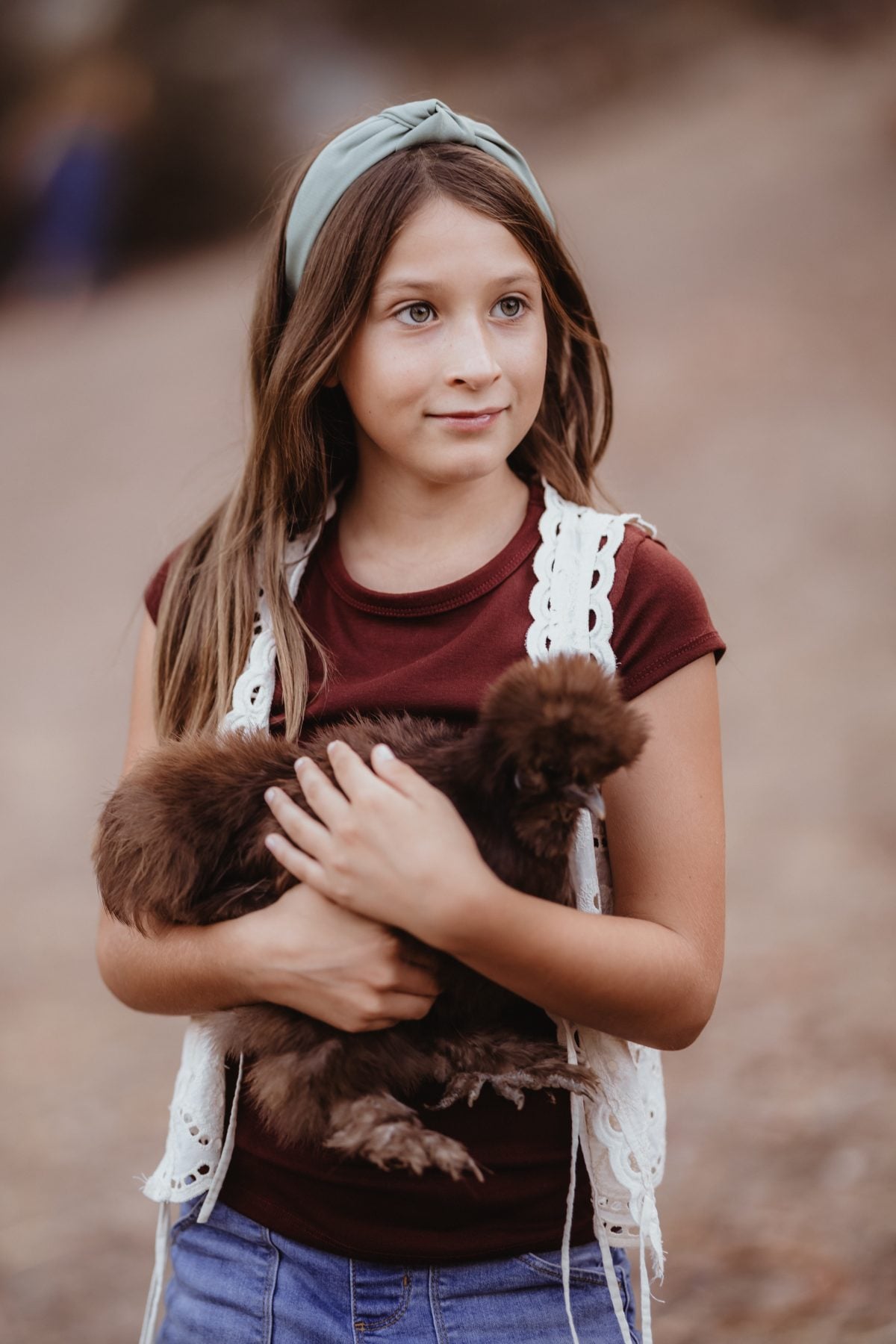 Girl in headband cradles a fluffy brown chicken in Lakeside, California