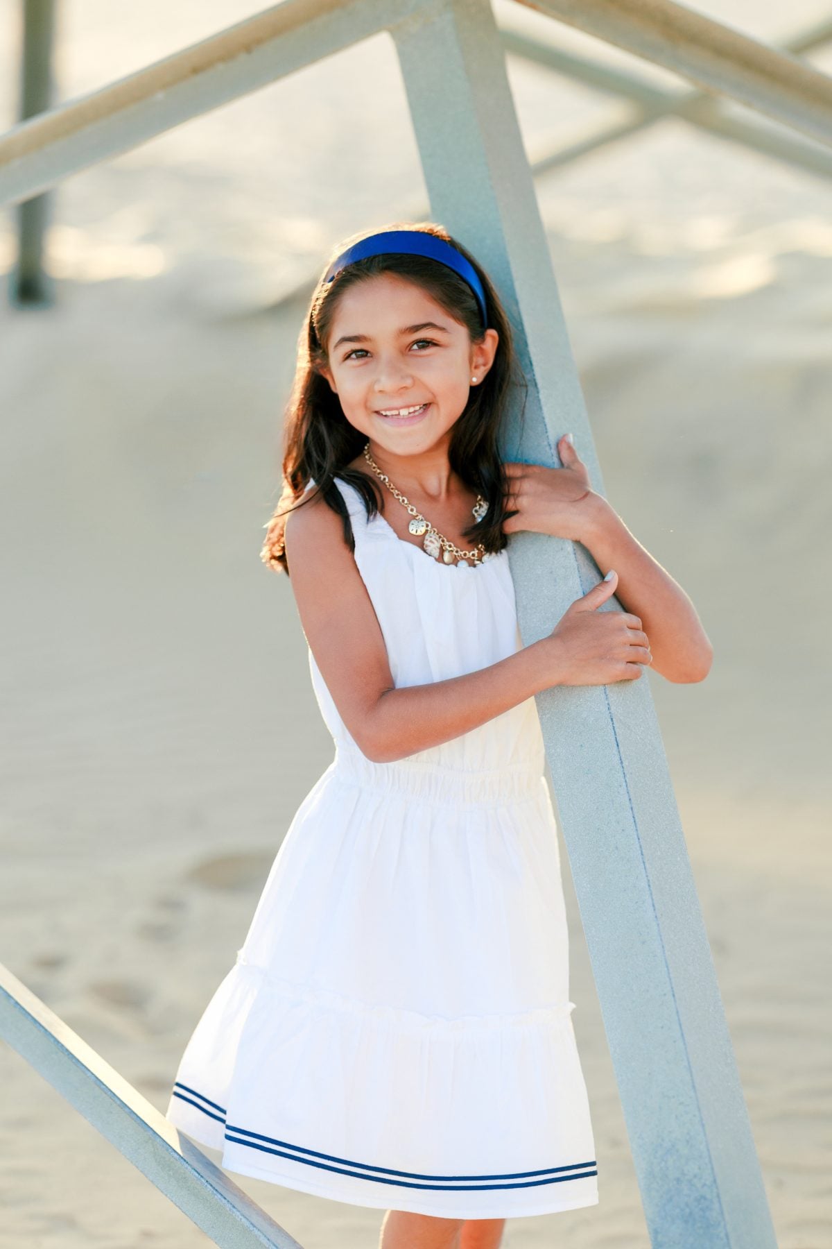 Girl in white dress leans against lifeguard tower rail, Coronado Beach