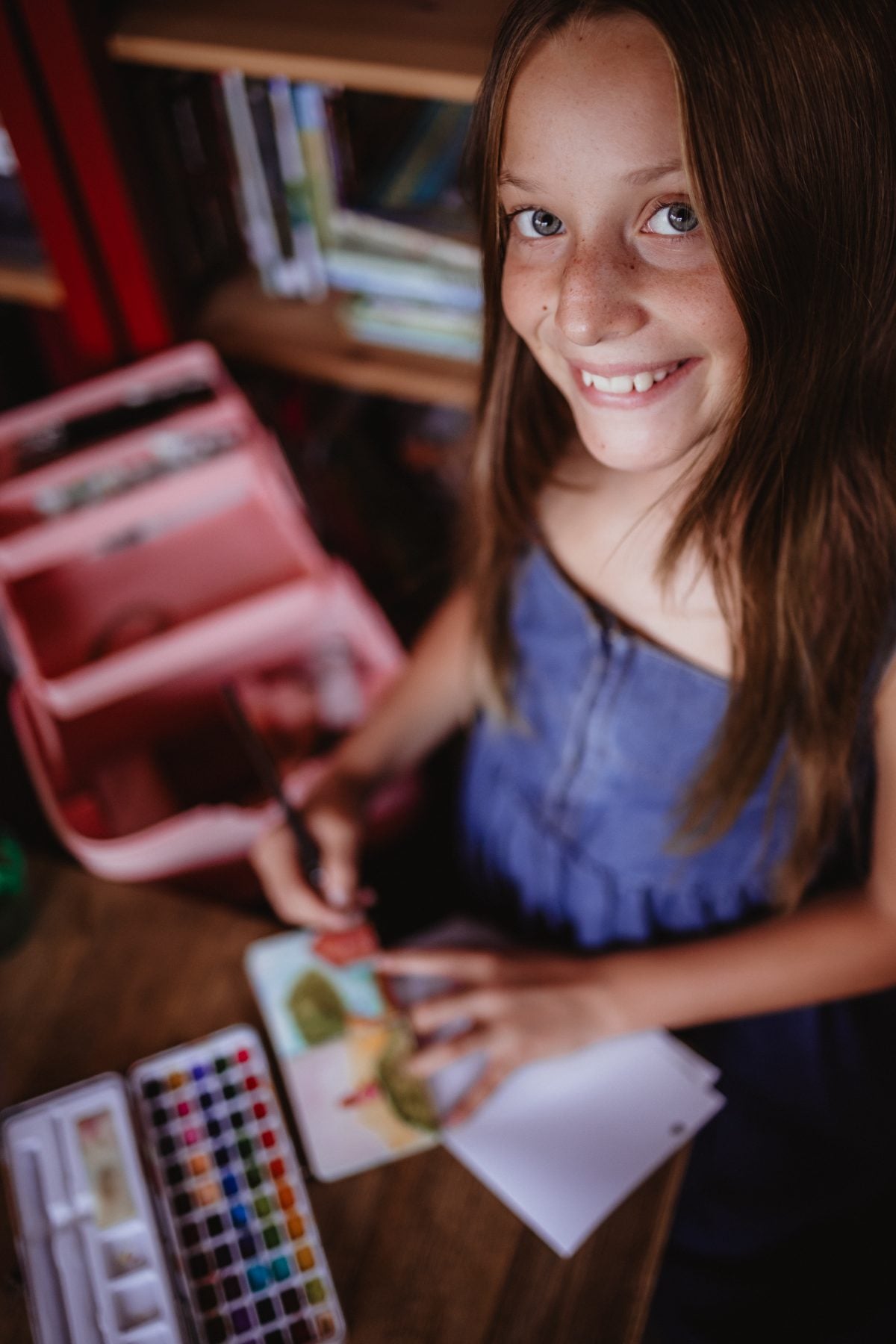 Young girl smiles while painting watercolors at a wooden desk