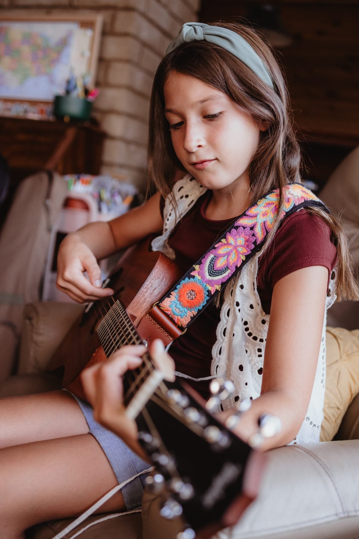 Girl playing acoustic guitar with colorful strap in living room