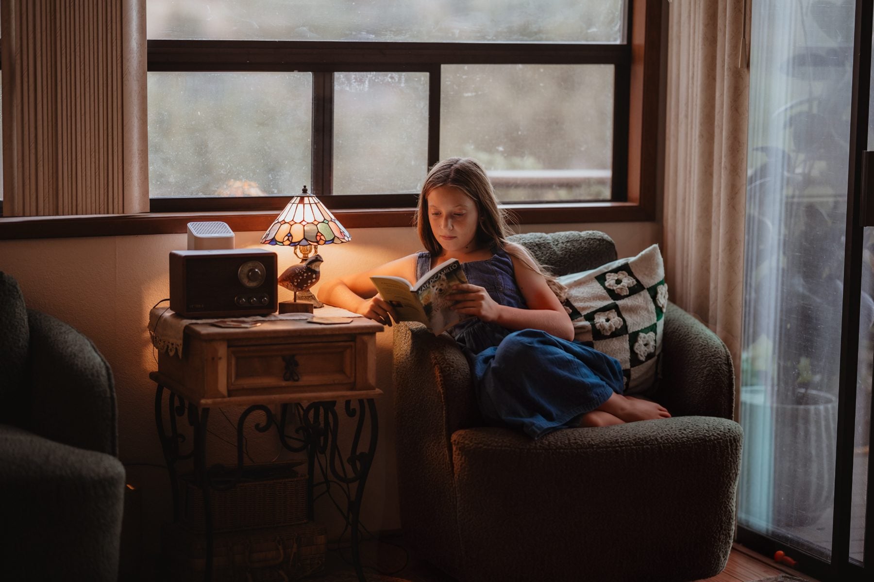 Girl reads a book by lamplight in cozy Lakeside armchair