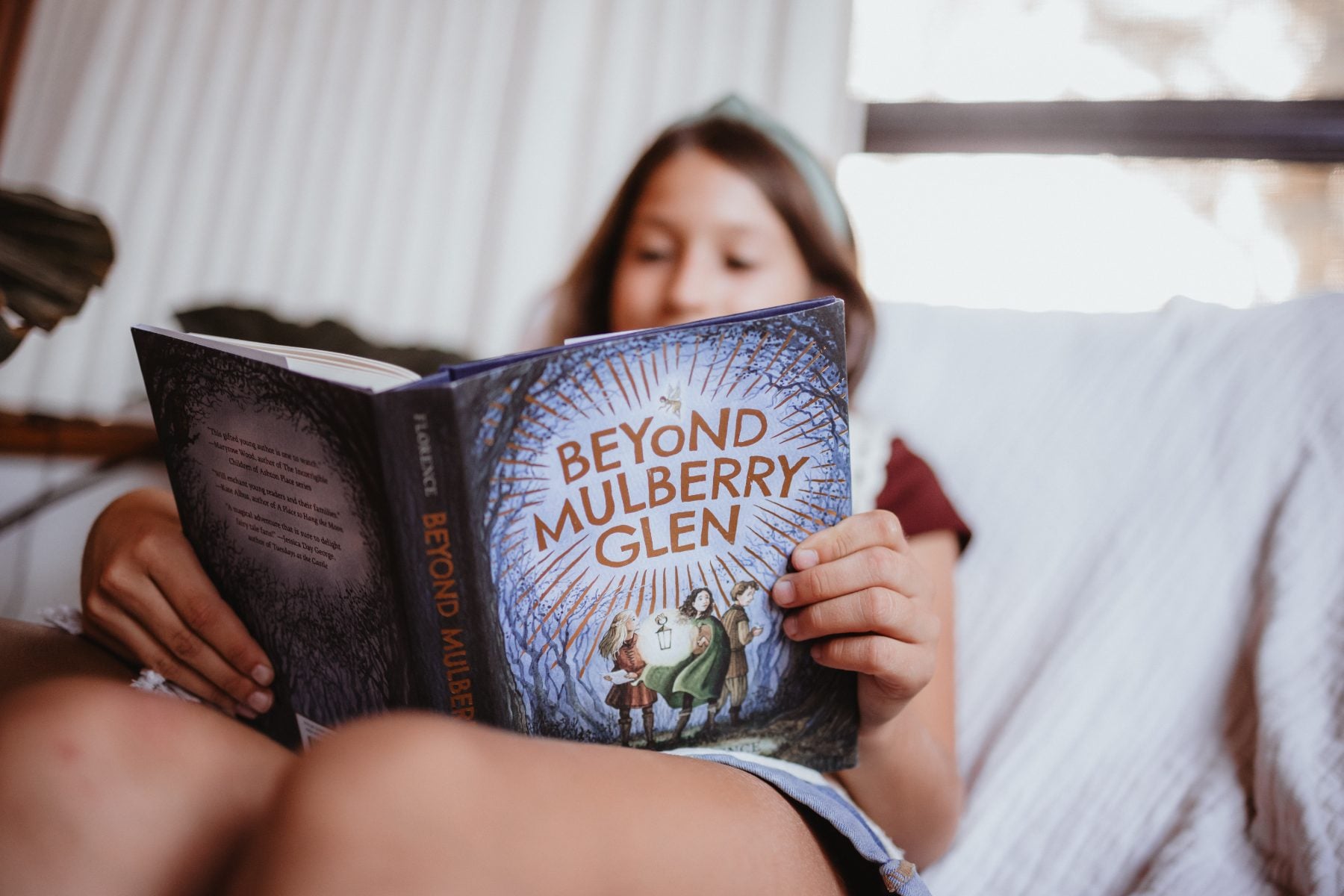 Girl reading Beyond Mulberry Glen curled up on the couch