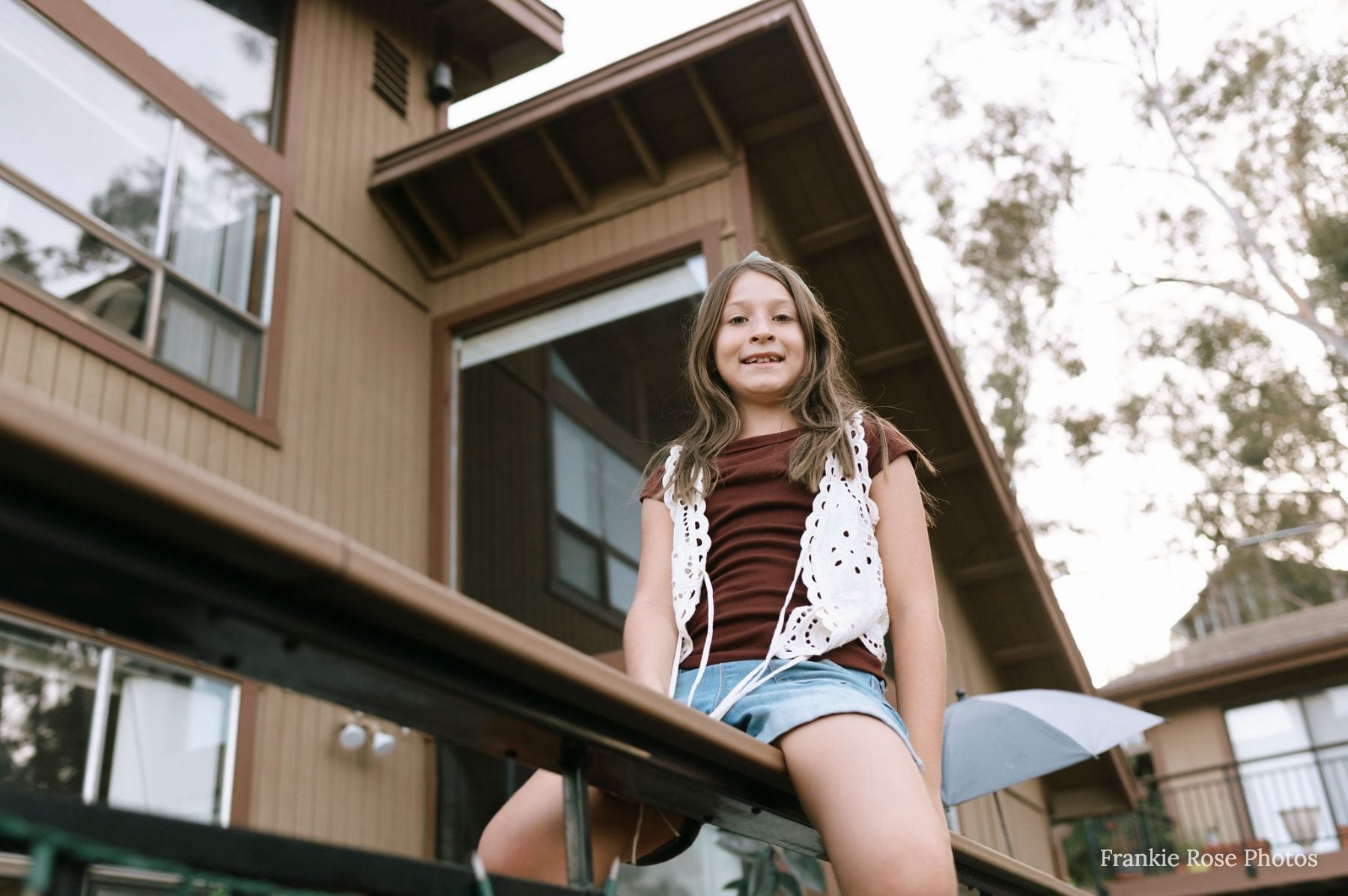 Girl sits smiling on a rooftop deck railing at the Lakeside family home