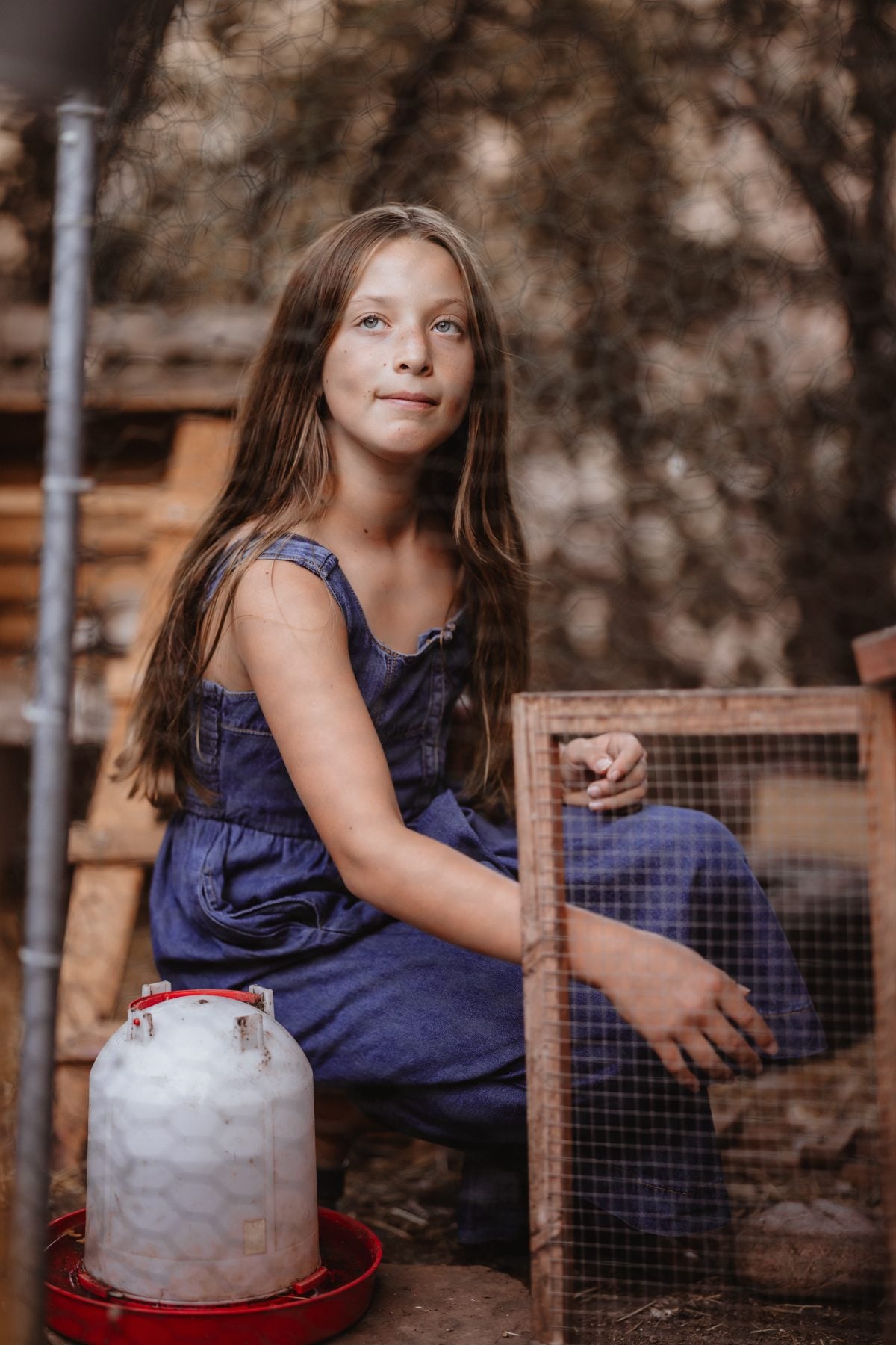 Girl rests near a wooden chicken coop and feeder in the backyard
