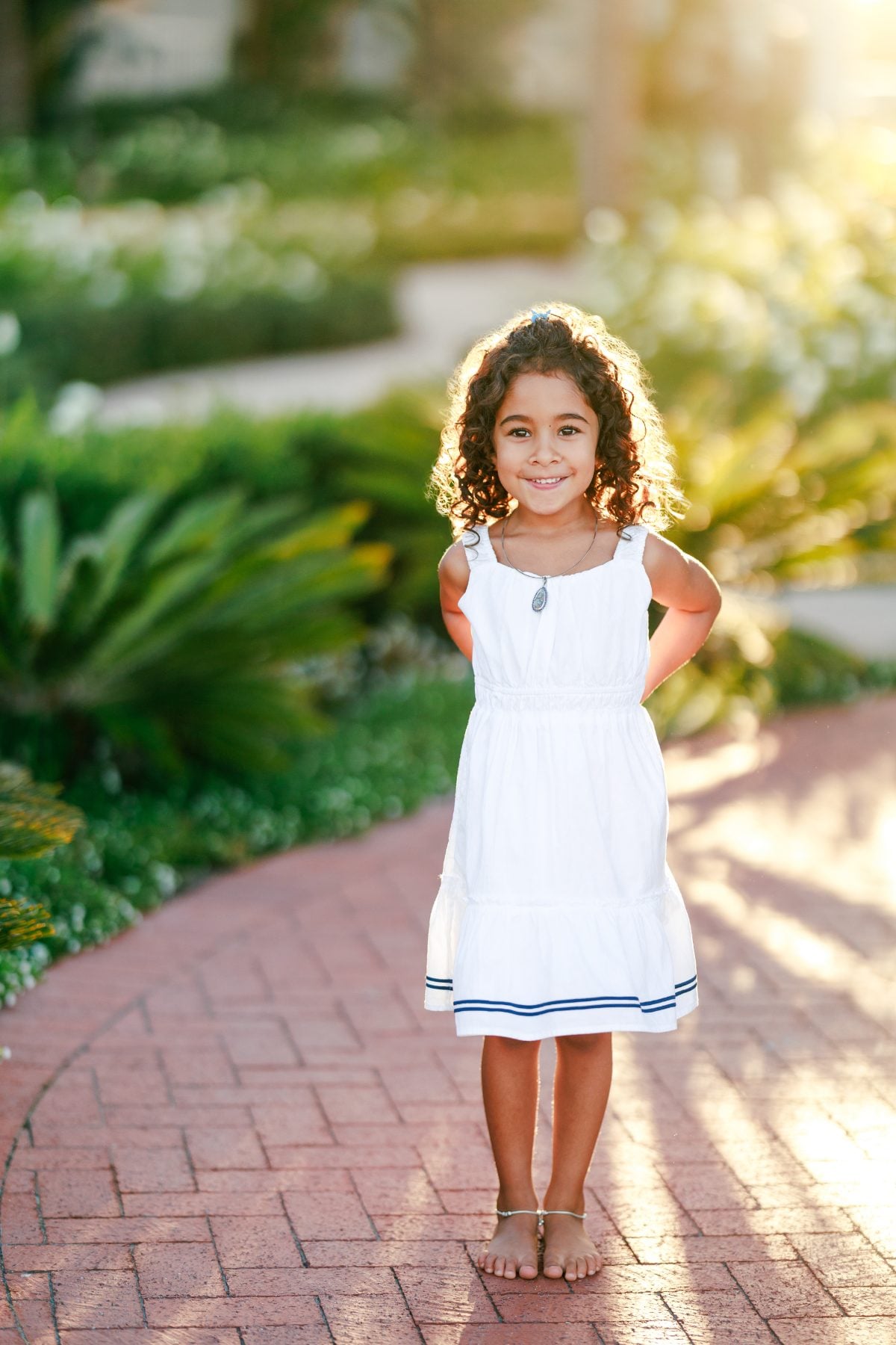 Young girl smiles while standing barefoot on a brick garden pathway