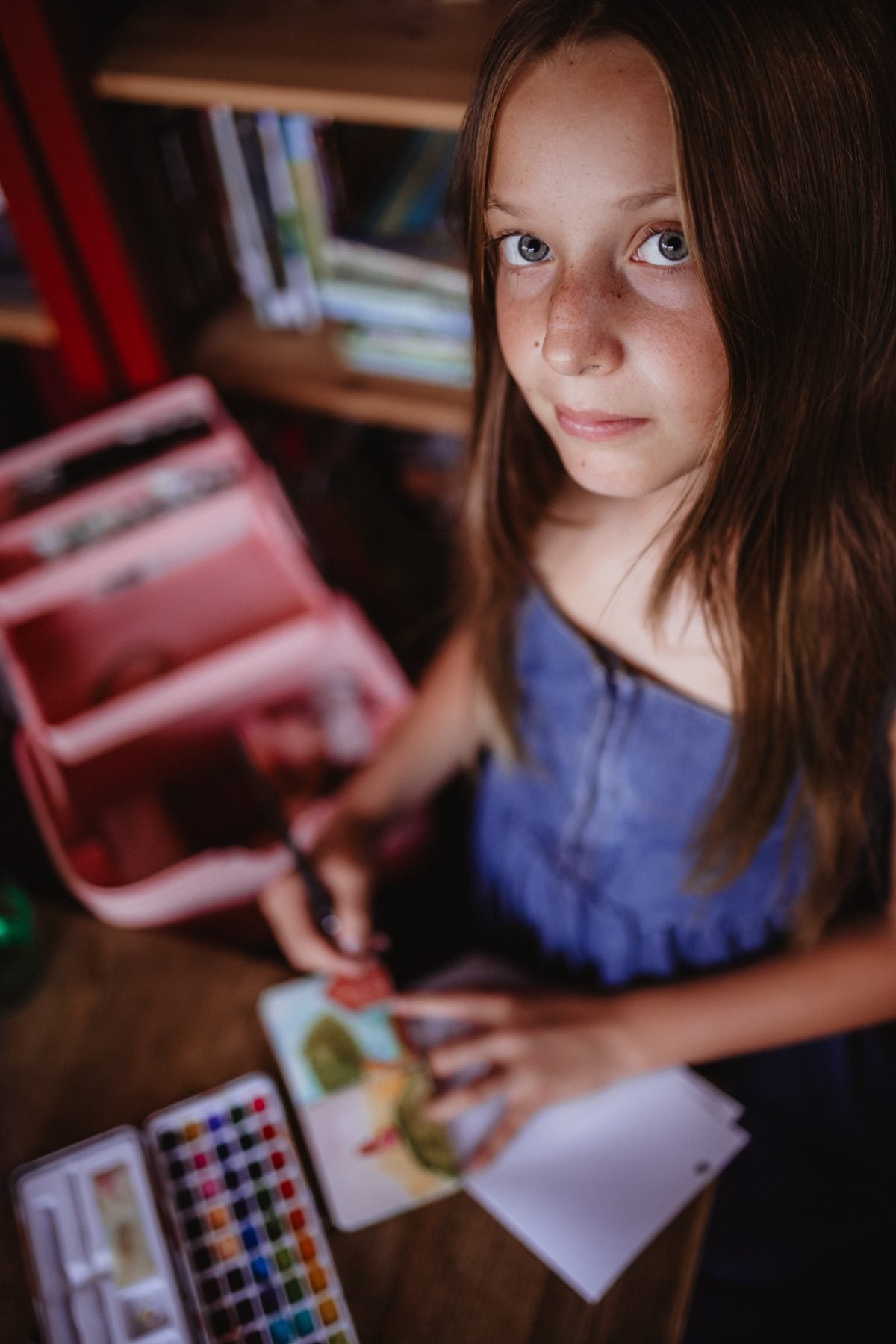 Girl pauses from watercolor painting to look up at the camera indoors