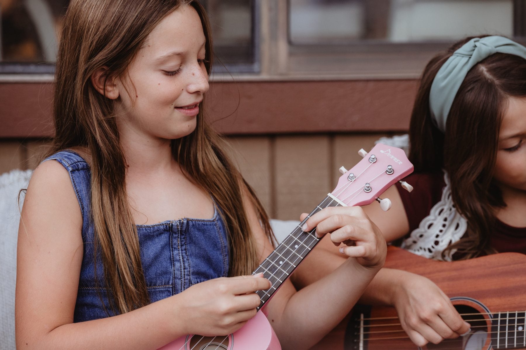 Girl smiles while strumming pink ukulele beside friend on guitar