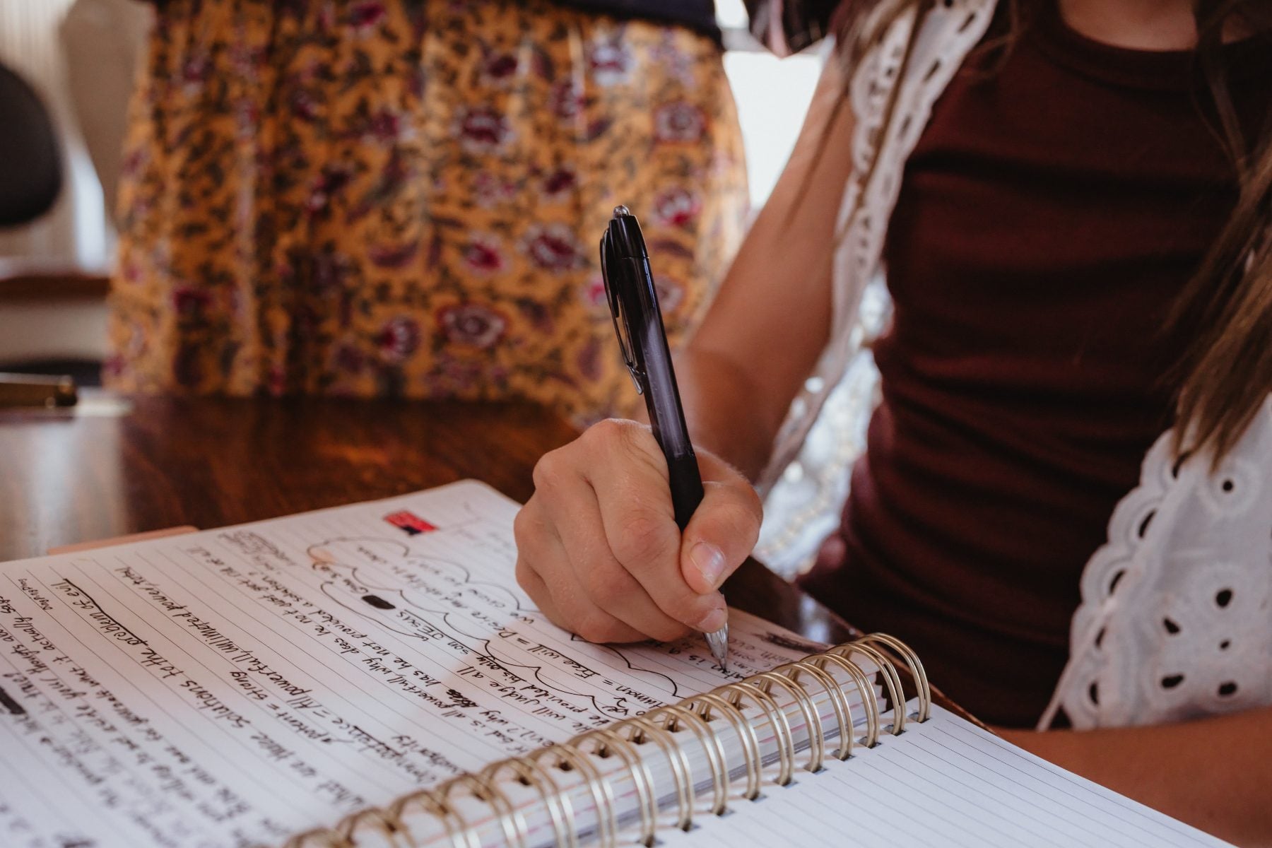 Hand writes notes in spiral notebook at wooden table