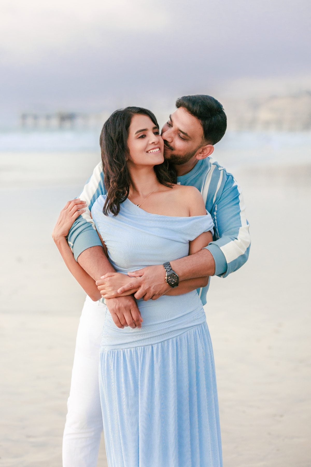 Husband kisses wife's cheek while embracing her on La Jolla beach