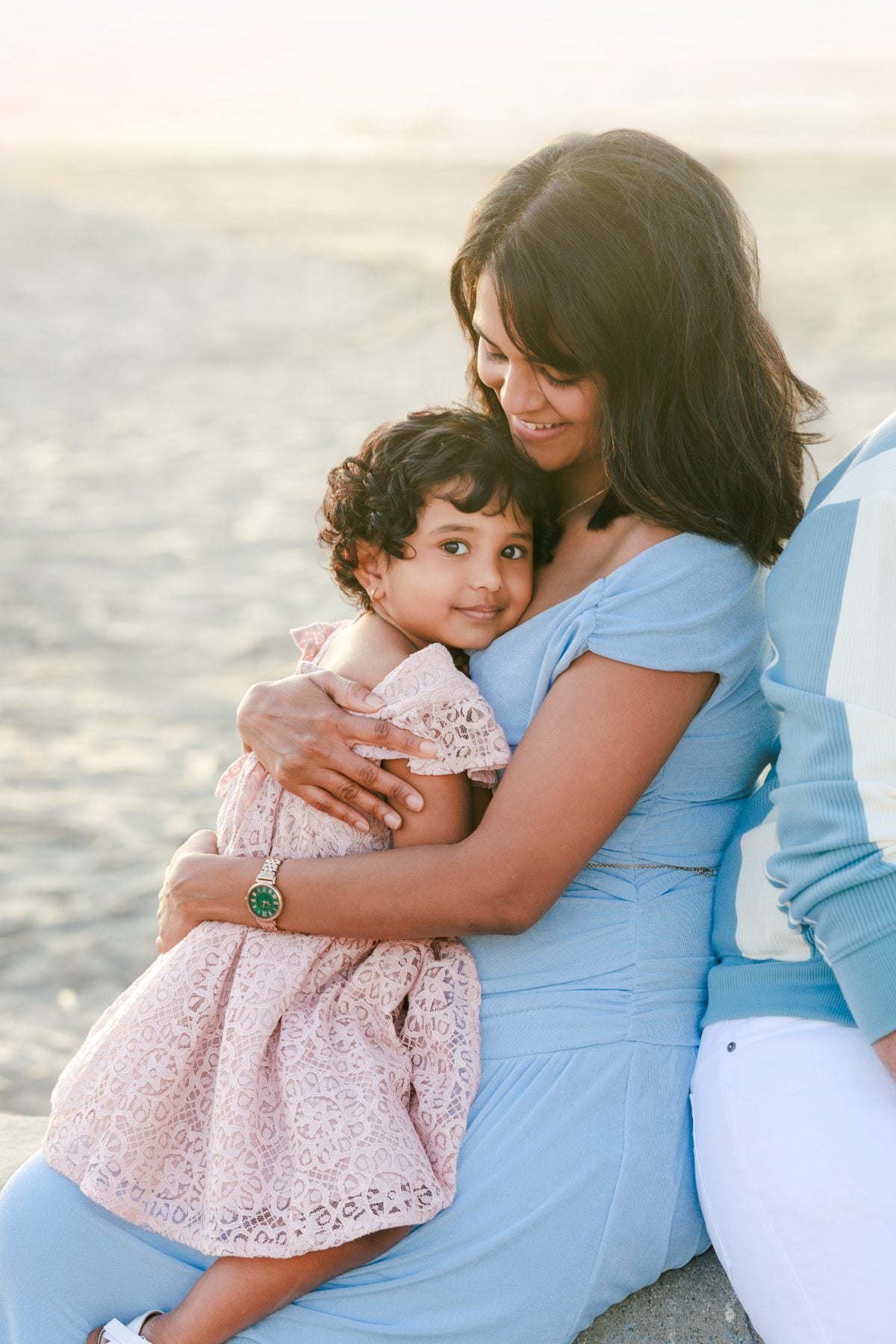 Mother cradles smiling toddler daughter against La Jolla Shores waves