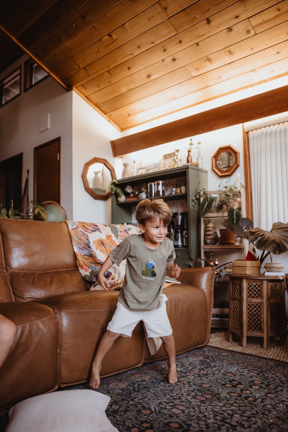 Barefoot boy dances beside couch under wood beam ceiling in Lakeside