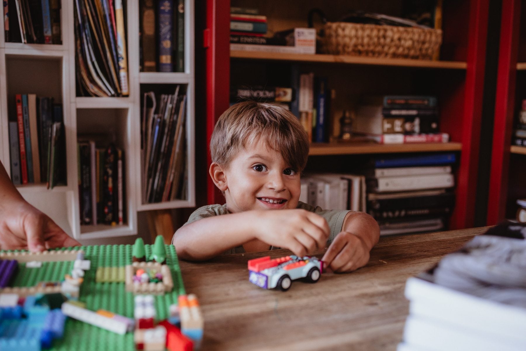 Smiling boy plays with Lego car at wooden table in Lakeside