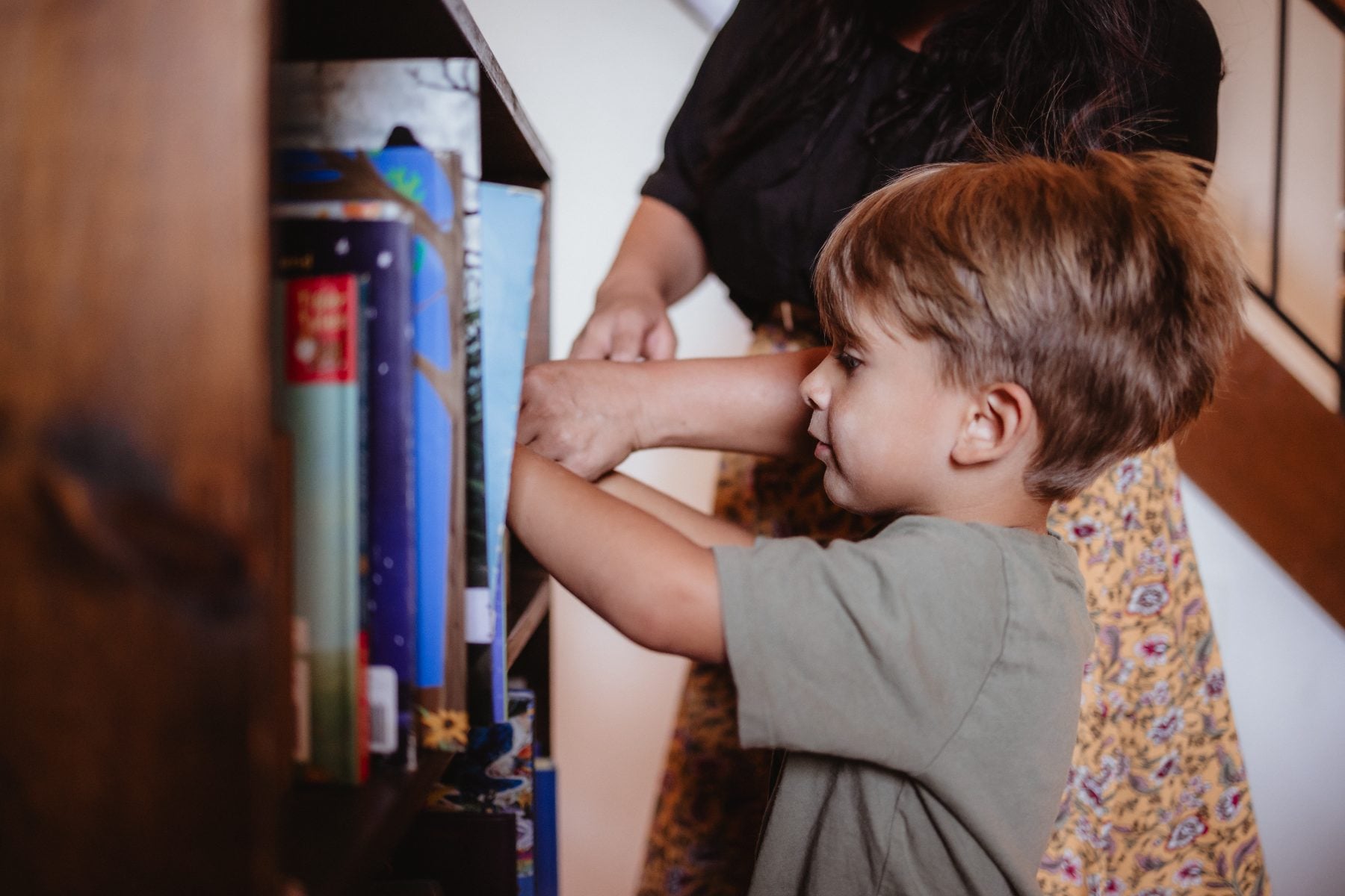 Boy reaches for storybooks on shelf while mom helps at Lakeside home