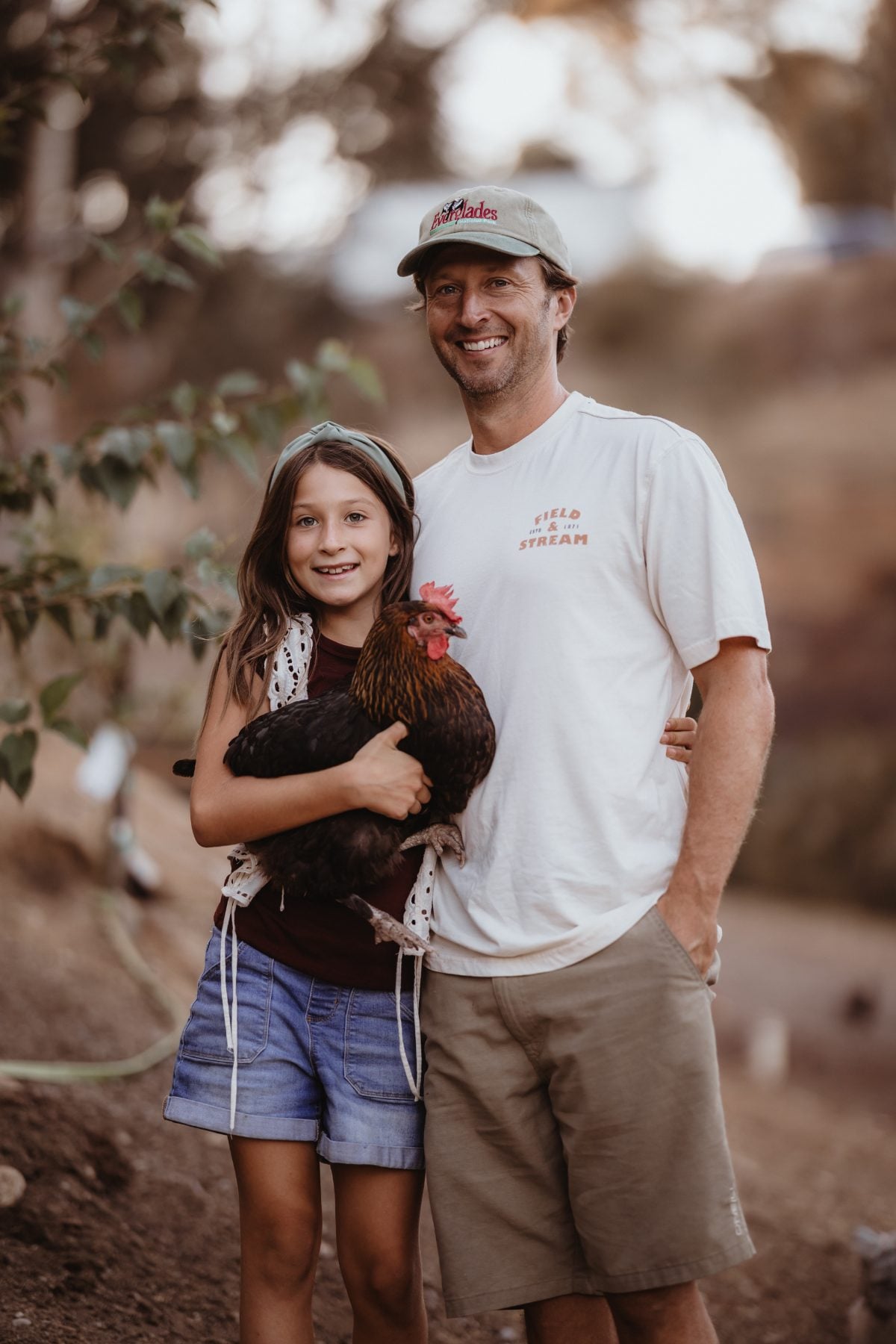 Dad and daughter smile at camera together while holding pet chicken