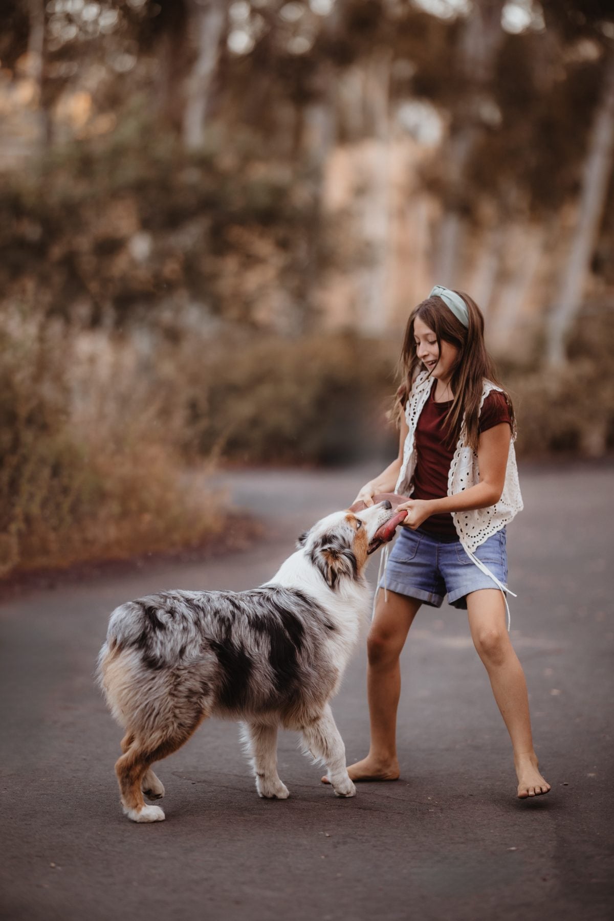 Girl bends down to pet her Australian shepherd on a path