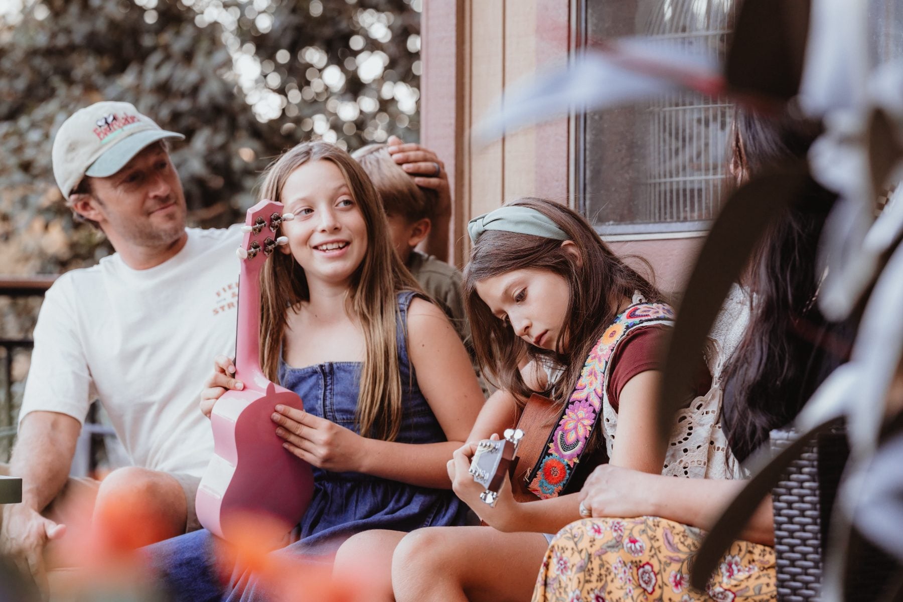Family gathers on porch as girl plays pink ukulele in Lakeside home