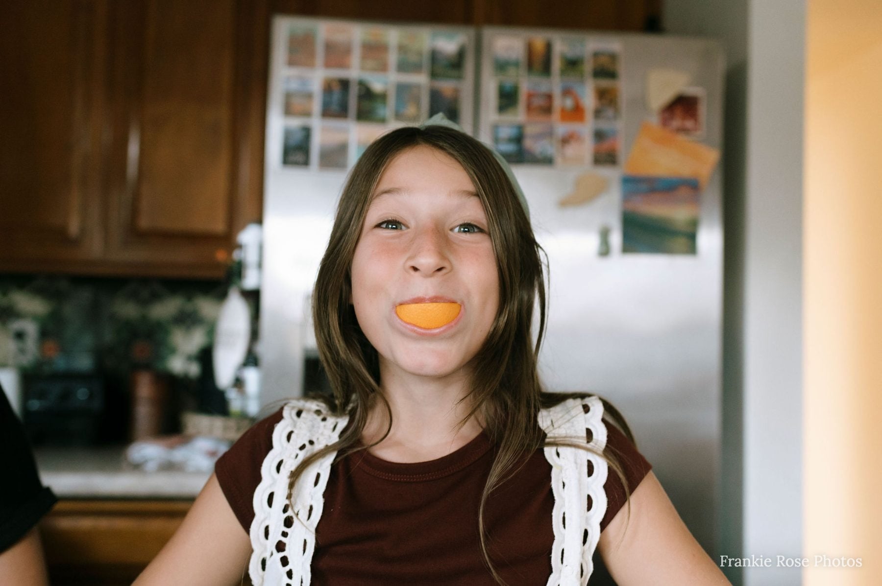 Girl balances an orange slice smile in a Lakeside kitchen, San Diego family photographer session