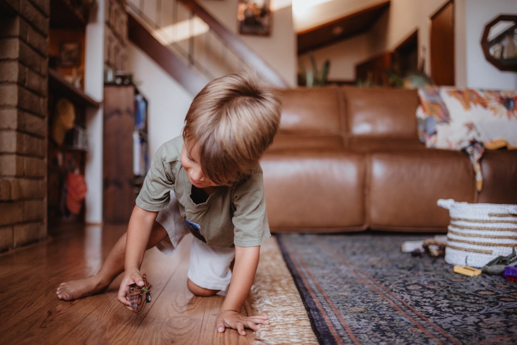 Barefoot boy kneels on floor near leather couch with toy