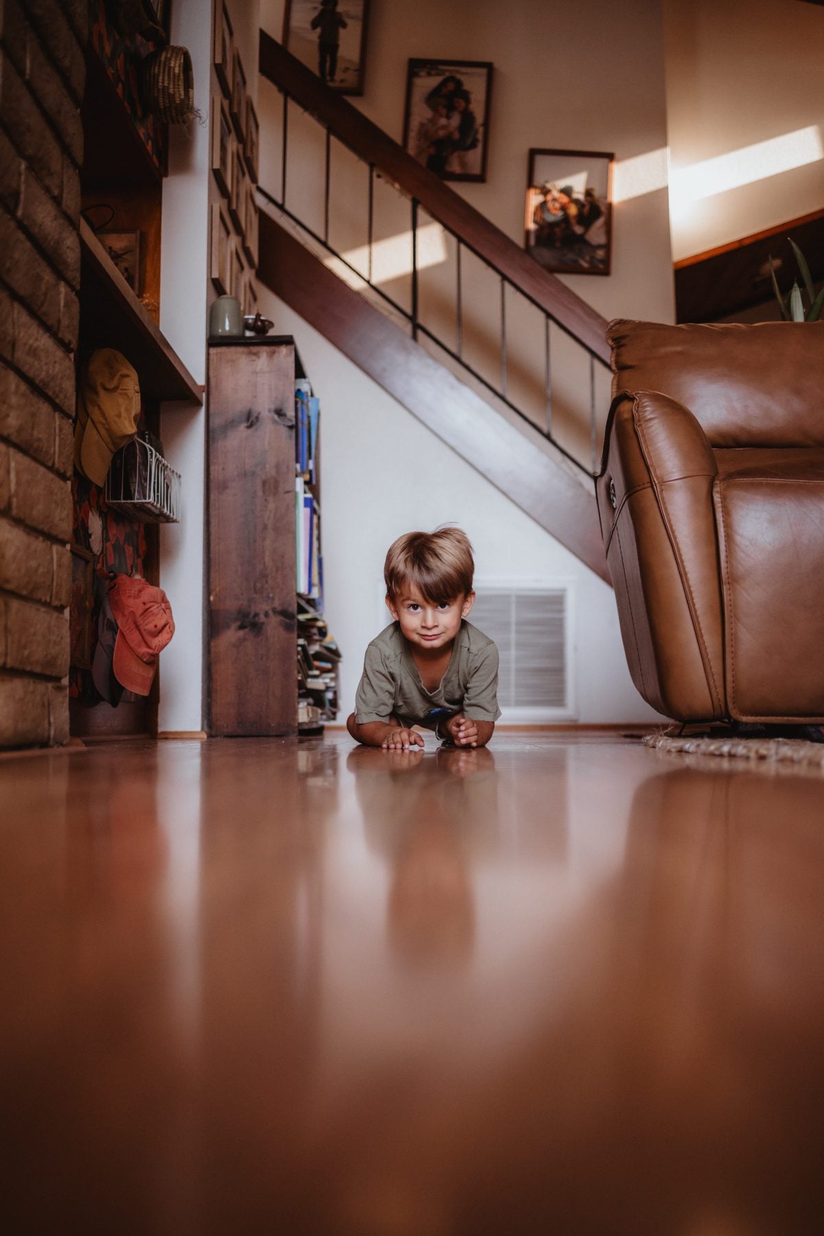 Boy lies flat on hardwood floor beside staircase at home