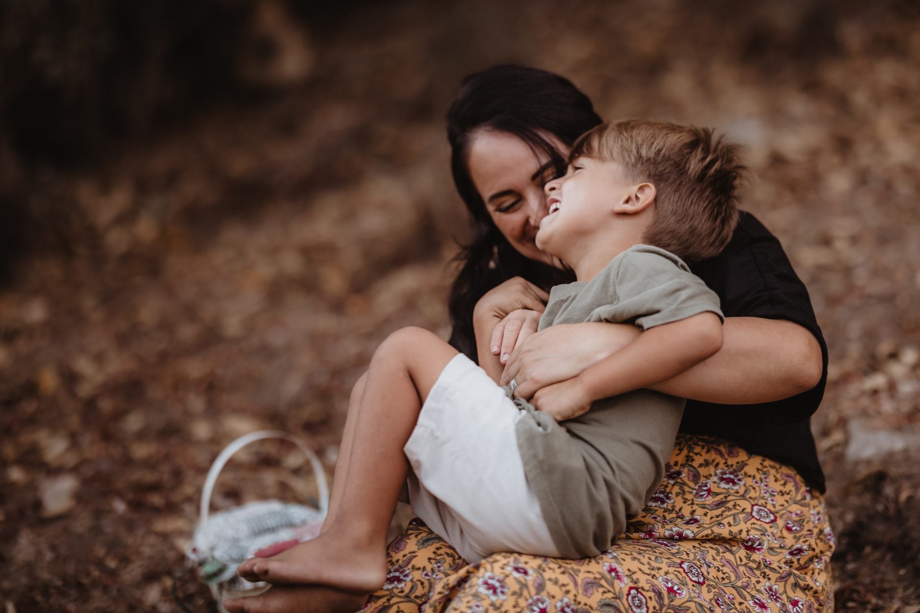Mother laughs nose-to-nose with young son sitting on her lap outside
