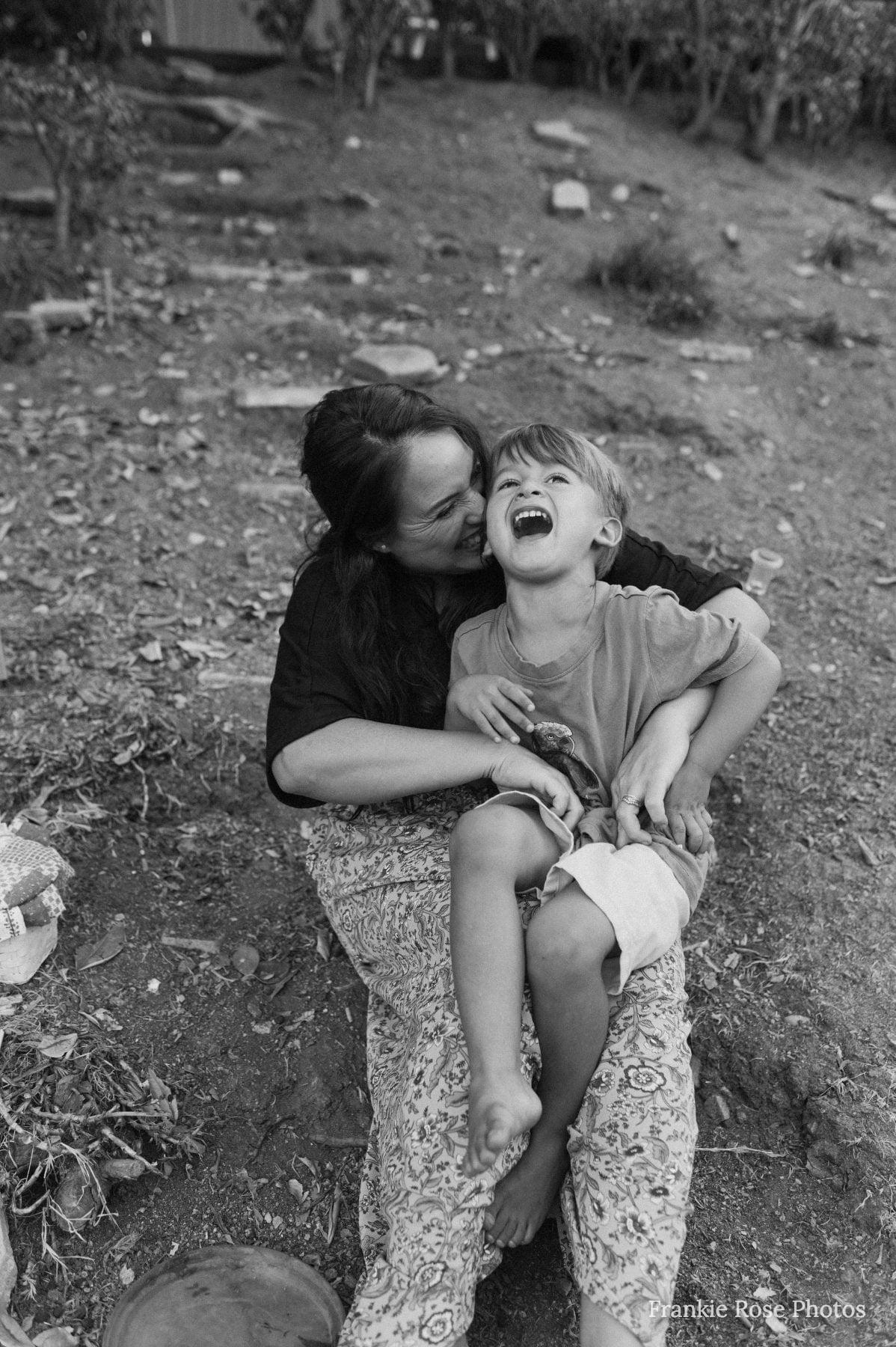 Mother laughs holding giggling child on lap outdoors in Lakeside