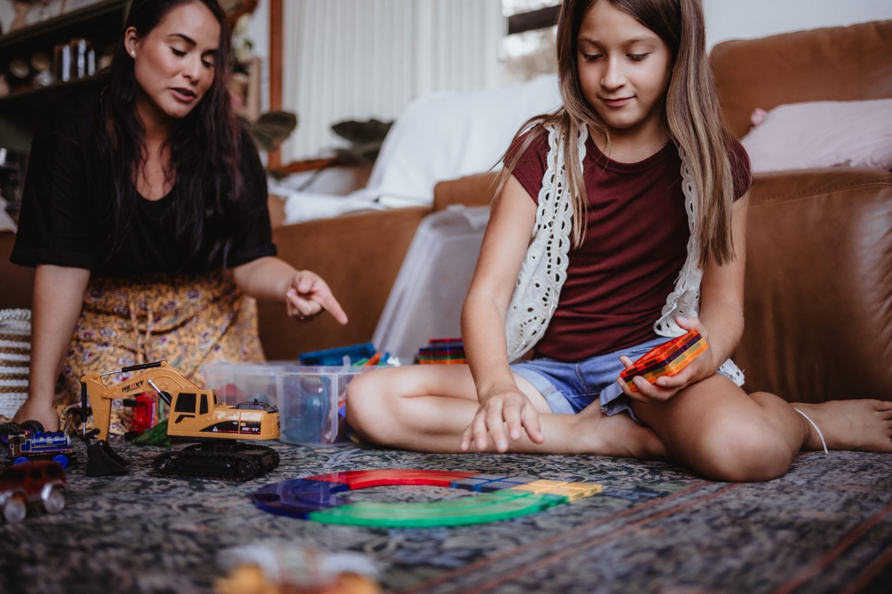 Mother and daughter play with toy trucks on the living room rug