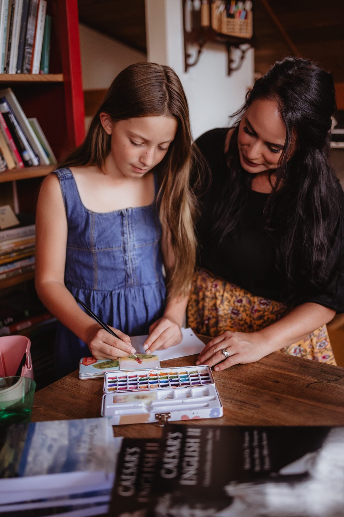 Mother guides daughter painting watercolors at a wooden table