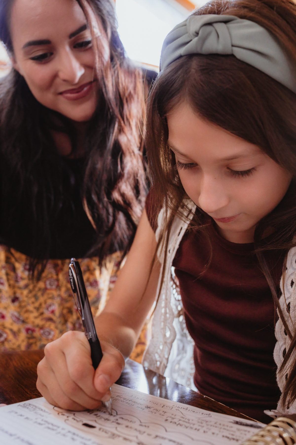 Close-up of mother helping daughter write carefully in notebook