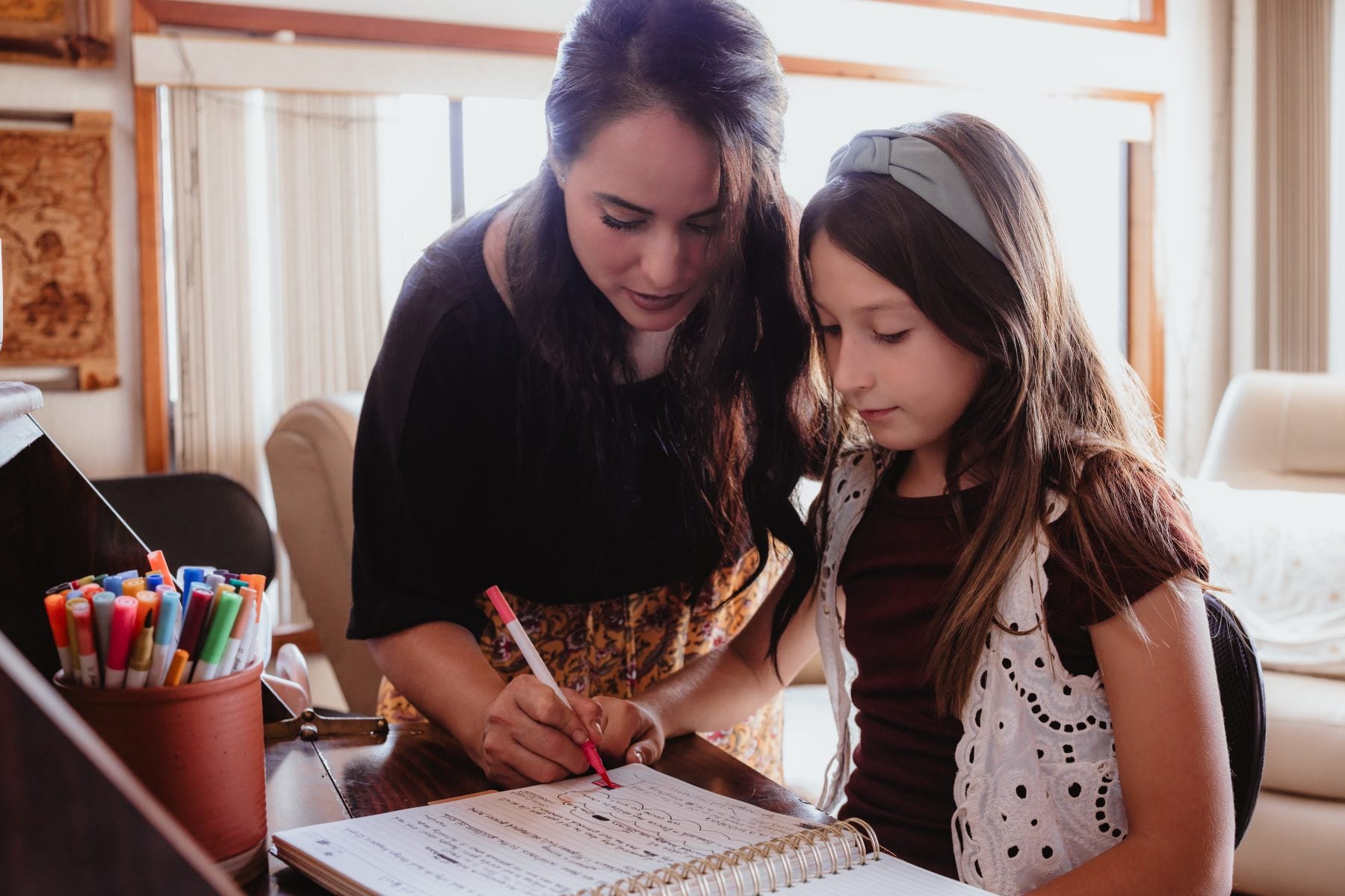 Mom guides daughter's hand with red marker while writing at piano