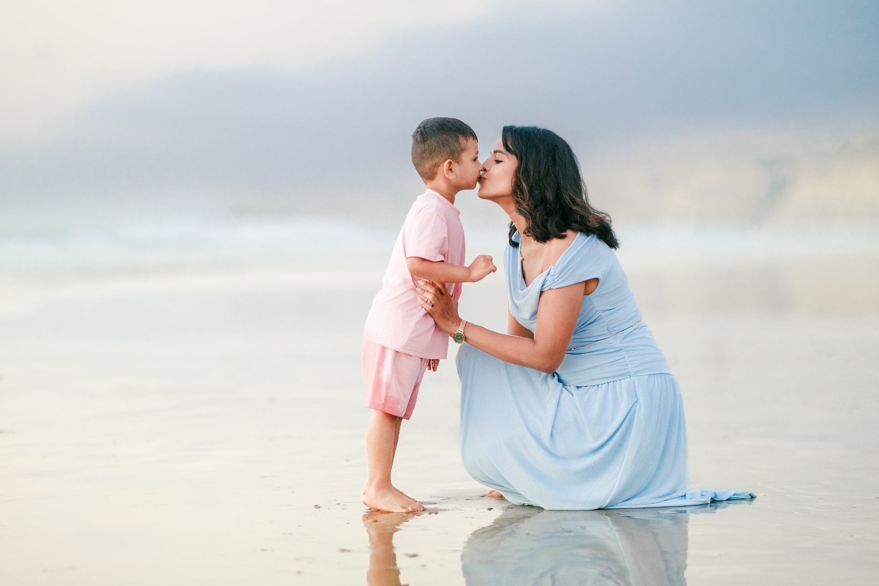 Mother kneels to kiss young son on sandy La Jolla Shores beach at sunset