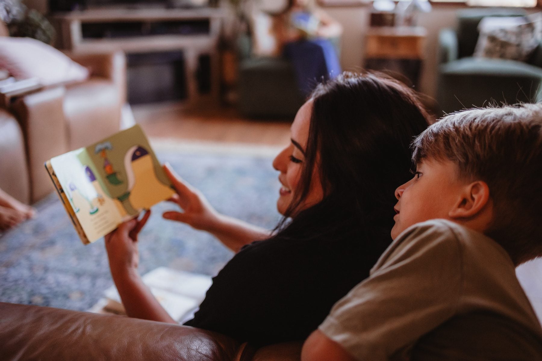 Mother reads a picture book aloud to her son on the couch