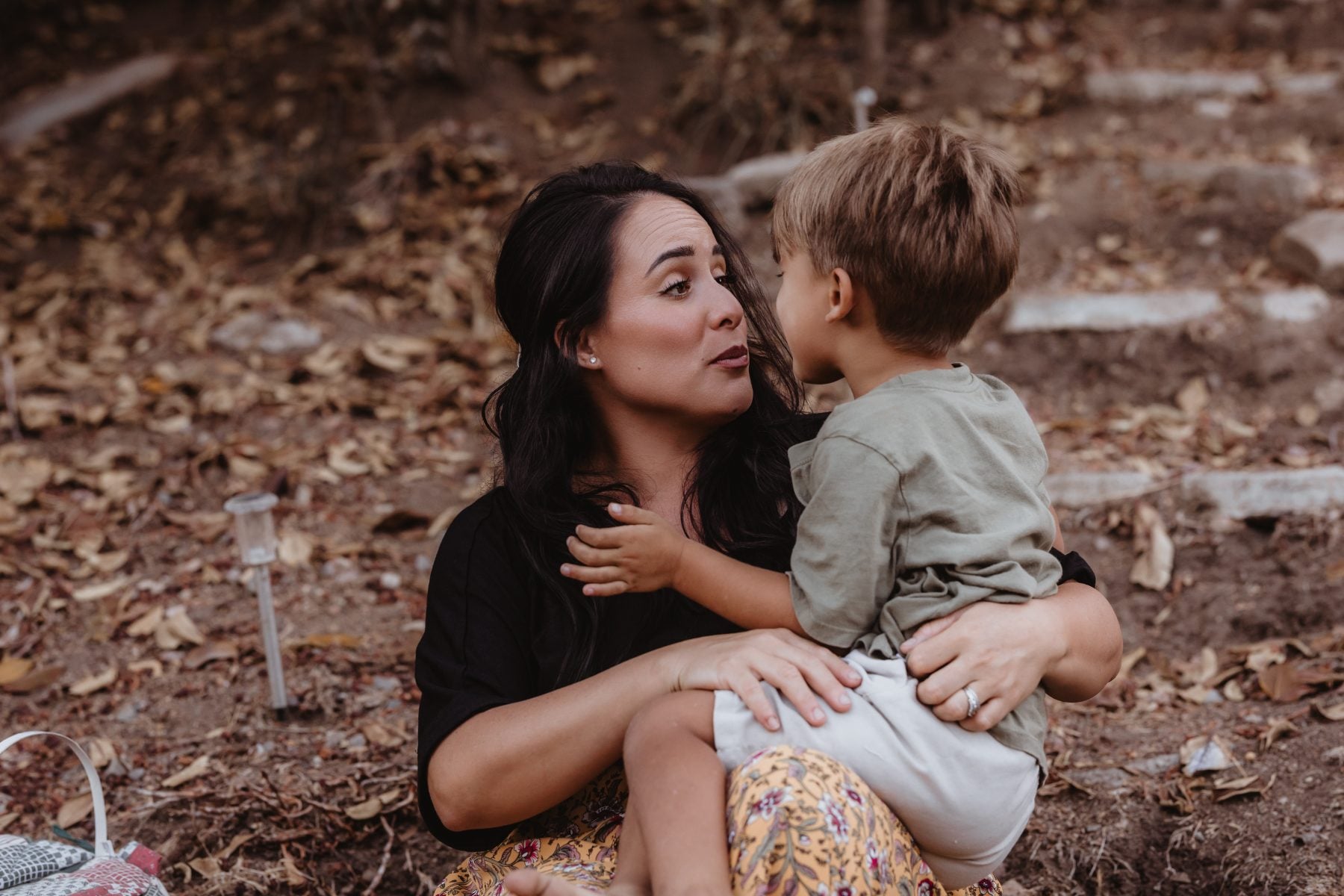 Mother and toddler son share a quiet moment outdoors among fallen leaves