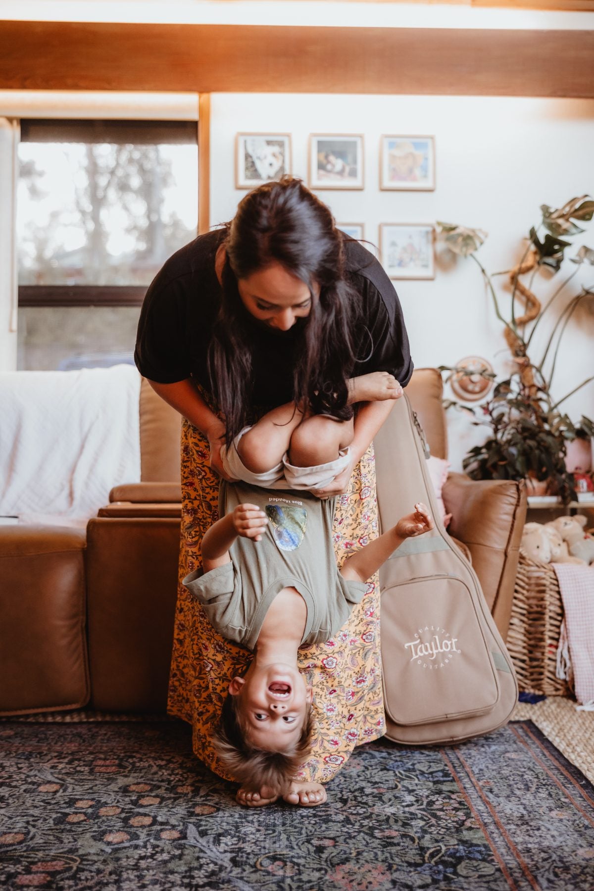 Mother playfully holds toddler upside down in living room