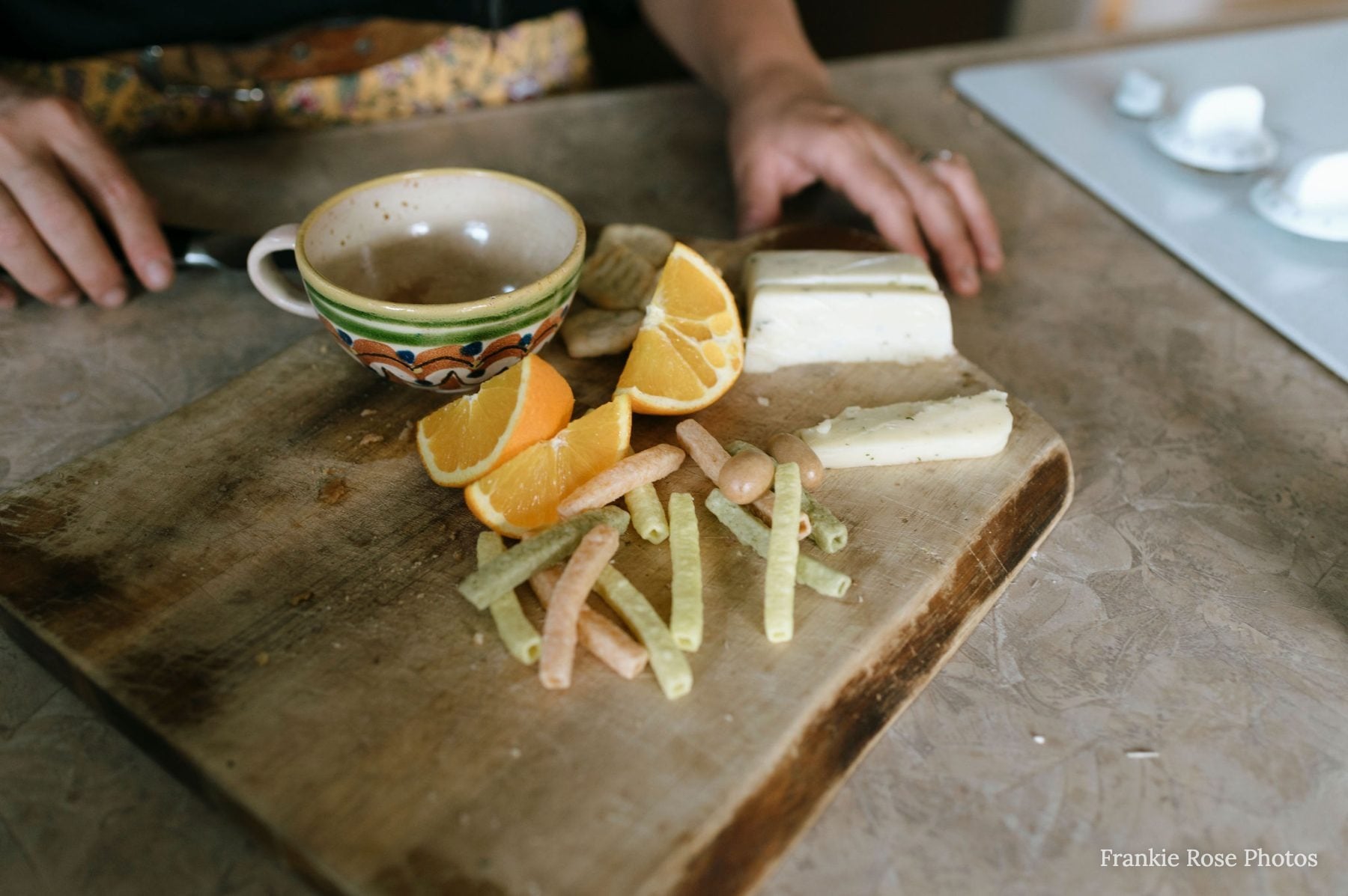 Hands arrange orange slices and cheese on a rustic cutting board at home