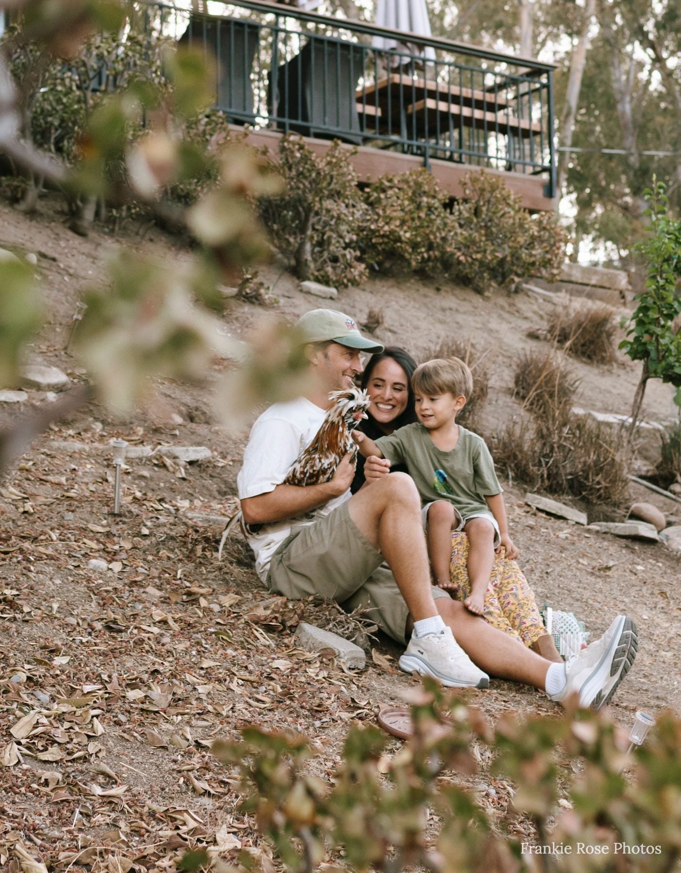 Parents sit on a hillside with their son holding a small toy giraffe