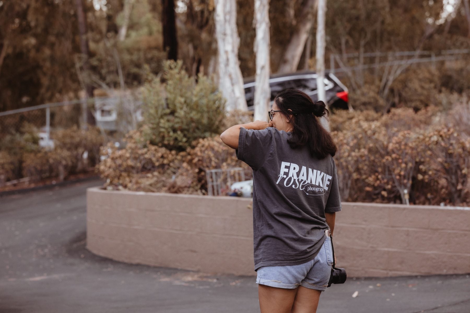 Photographer in Frankie Rose shirt stands outdoors near parked car