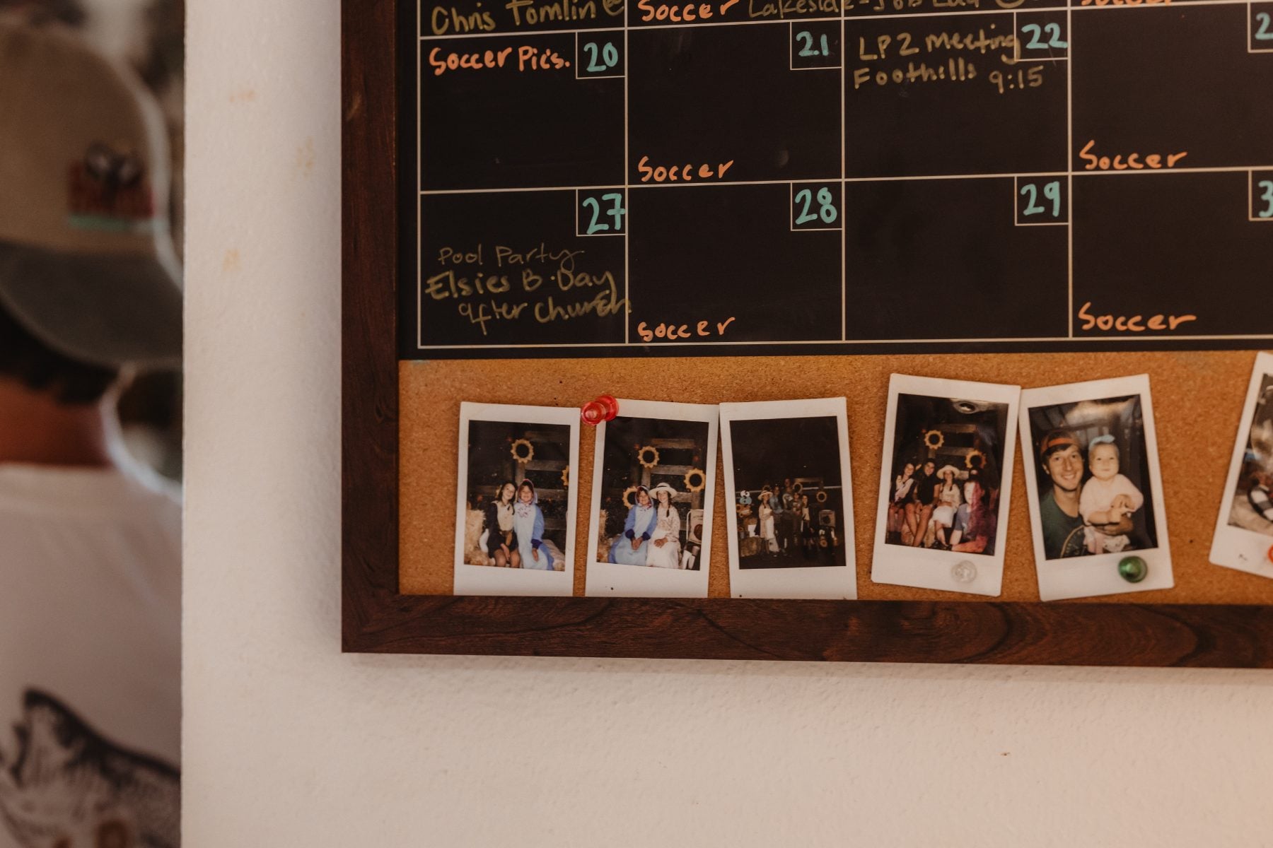 Corkboard displays framed Polaroid family photos beside soccer calendar