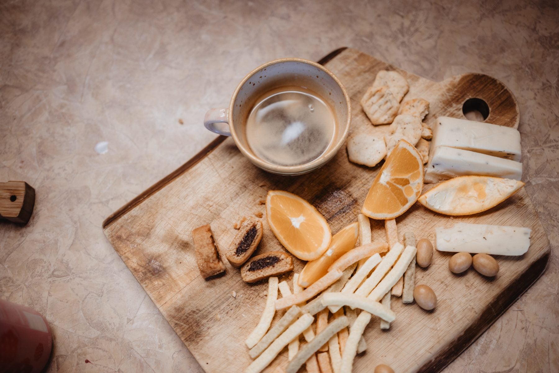 Rustic board with coffee, cheese, orange slices, and almonds