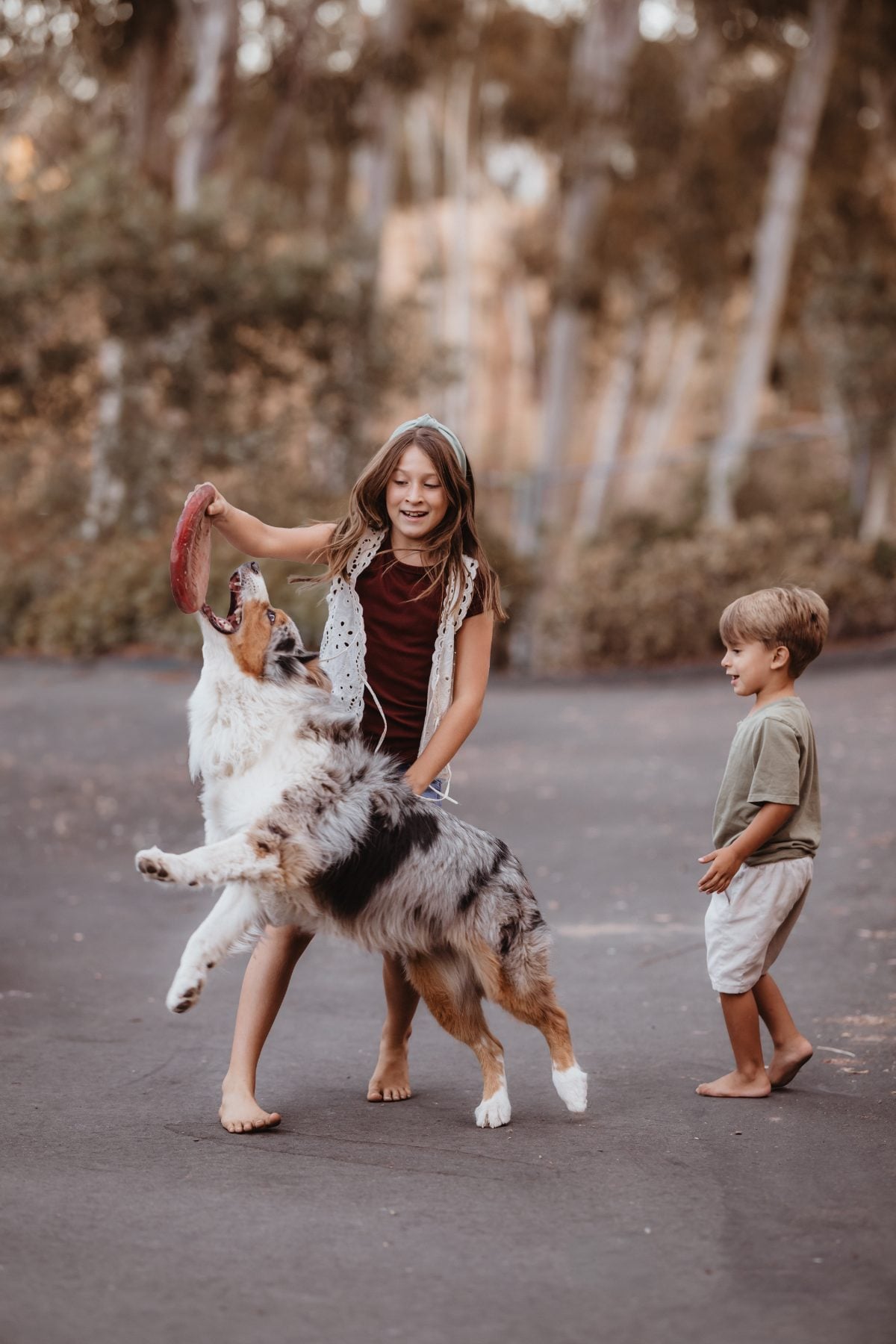 Girl laughs while a dog leaps beside her brother on the driveway in Lakeside