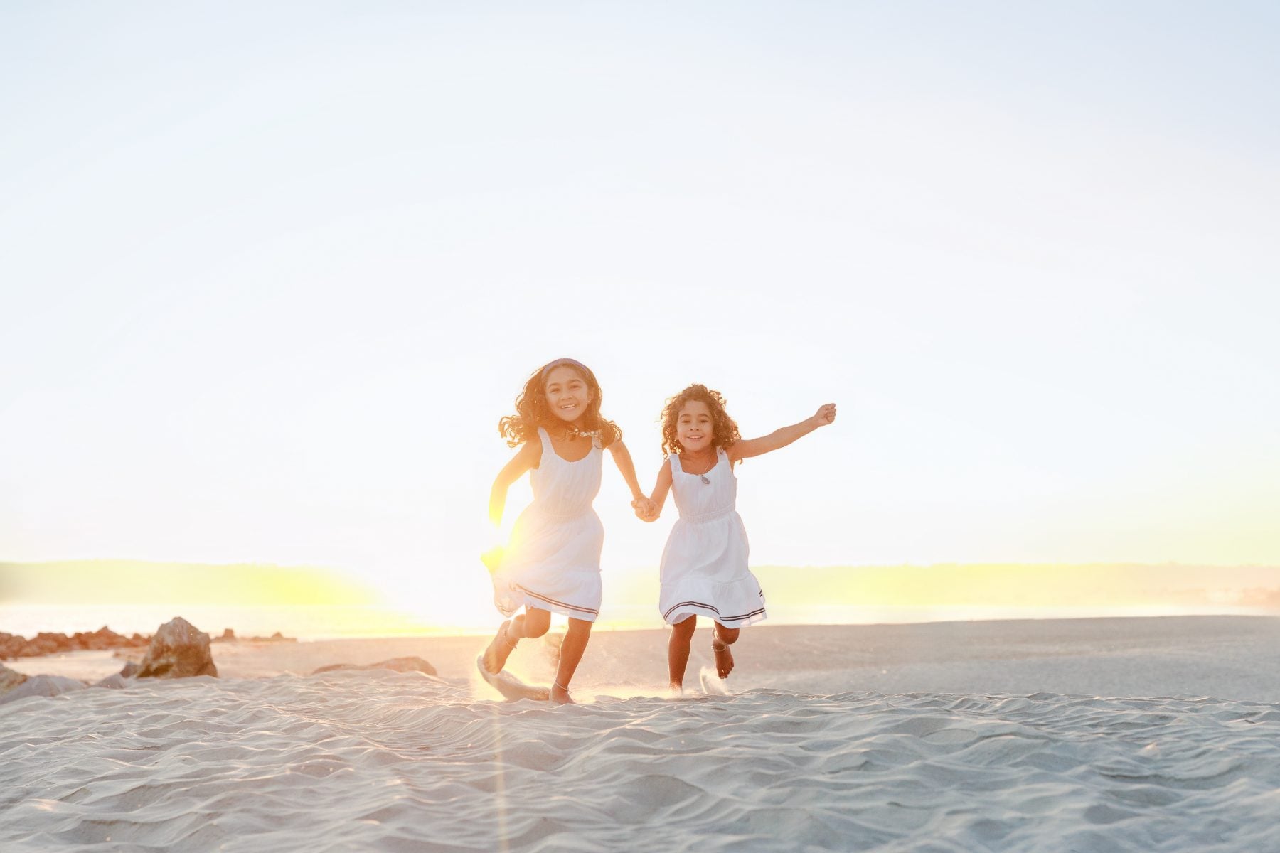 Two sisters hold hands running along the shoreline at sunset