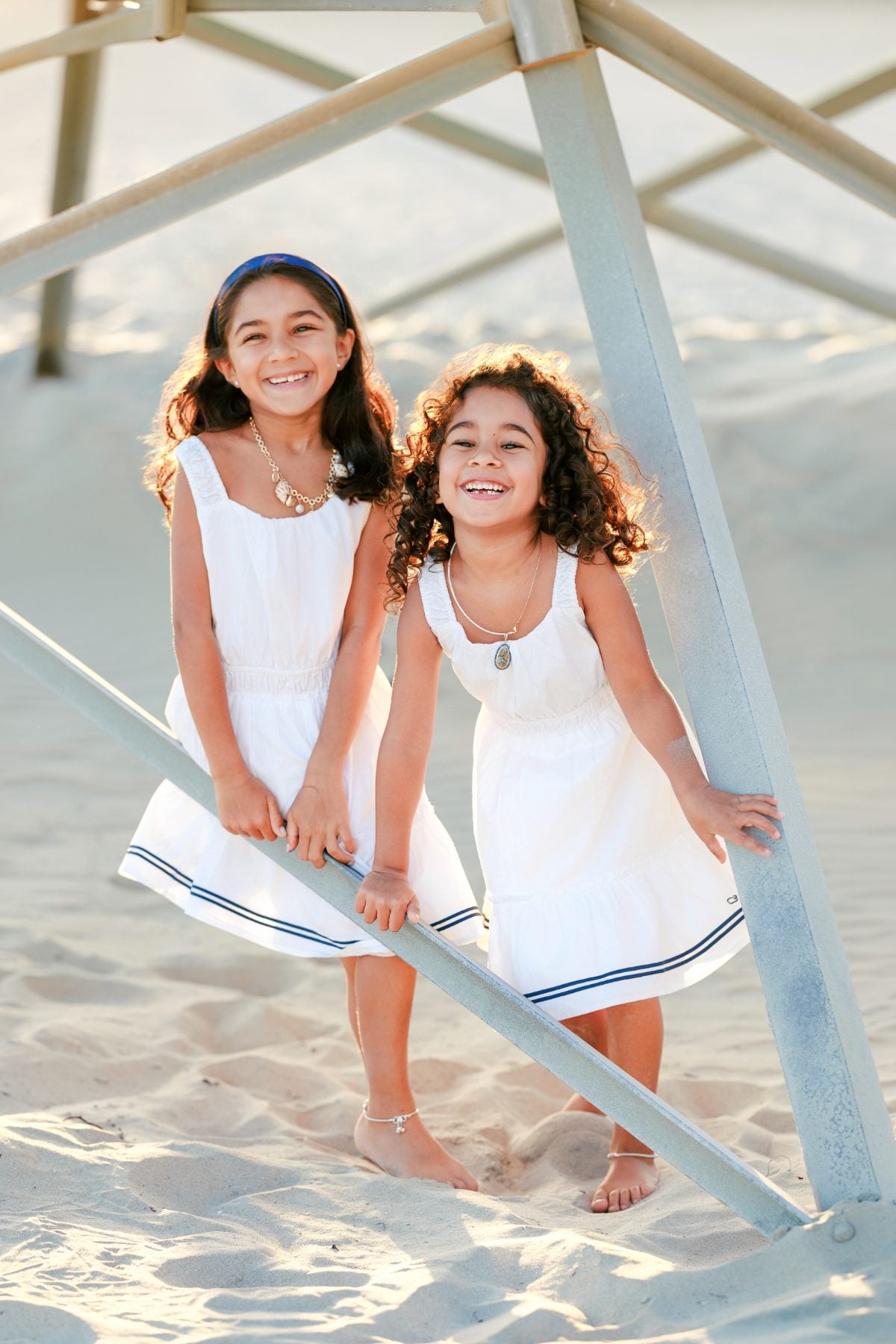 Two barefoot sisters smile together under beach lifeguard tower